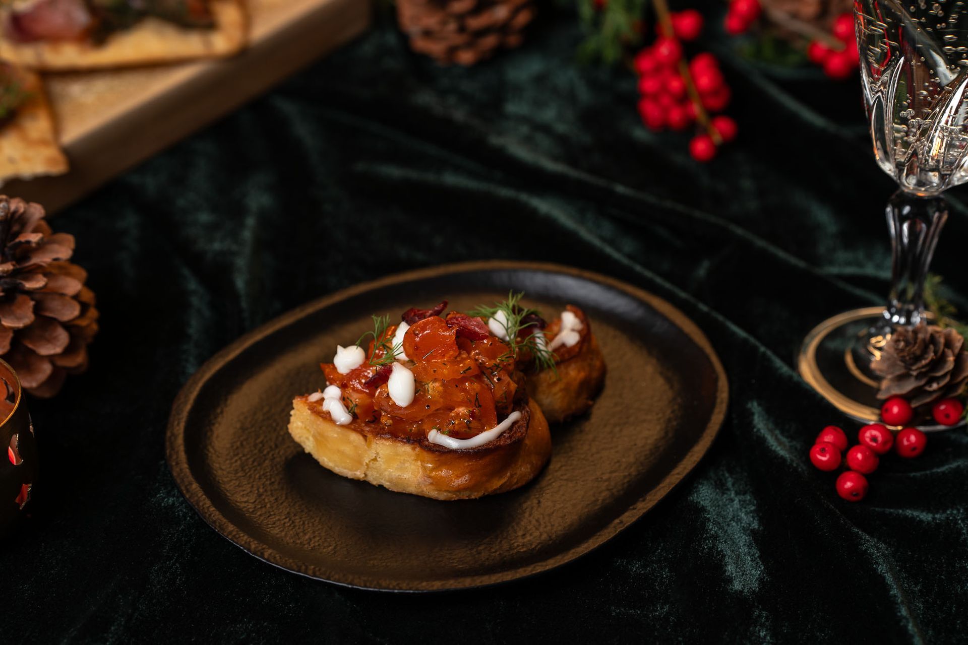 Tveir litlir forréttir á dökkum diski, hátíðlegur umgjörð með grænmeti og glasi af kampavíni.