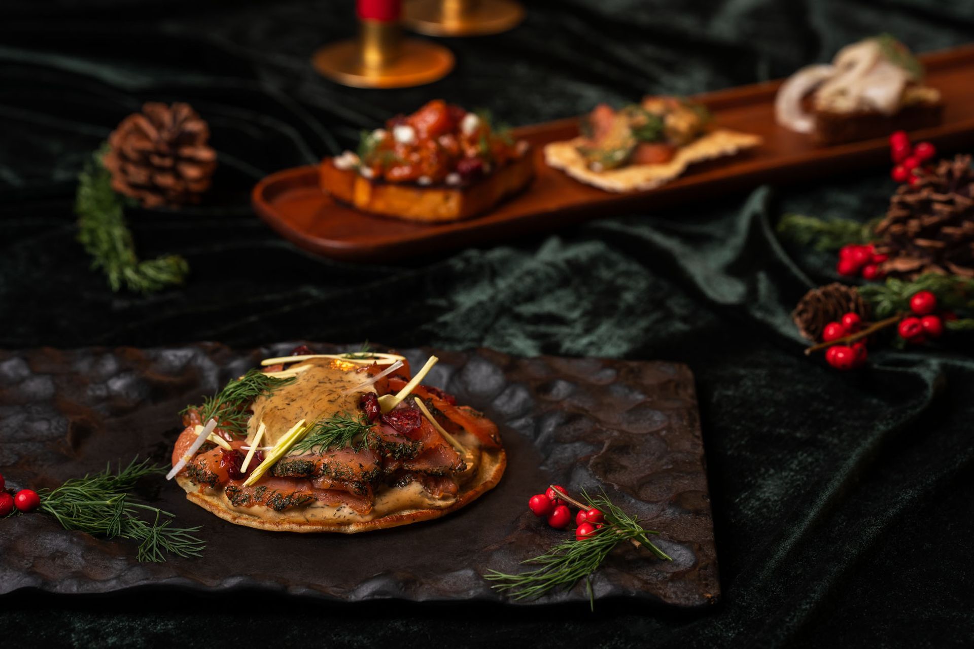 Lúxus forréttir á dökkum diski, hátíðlegur staður. Brauð með hráefnum, furukönglum, rauðum berjum og grænu grænmeti.