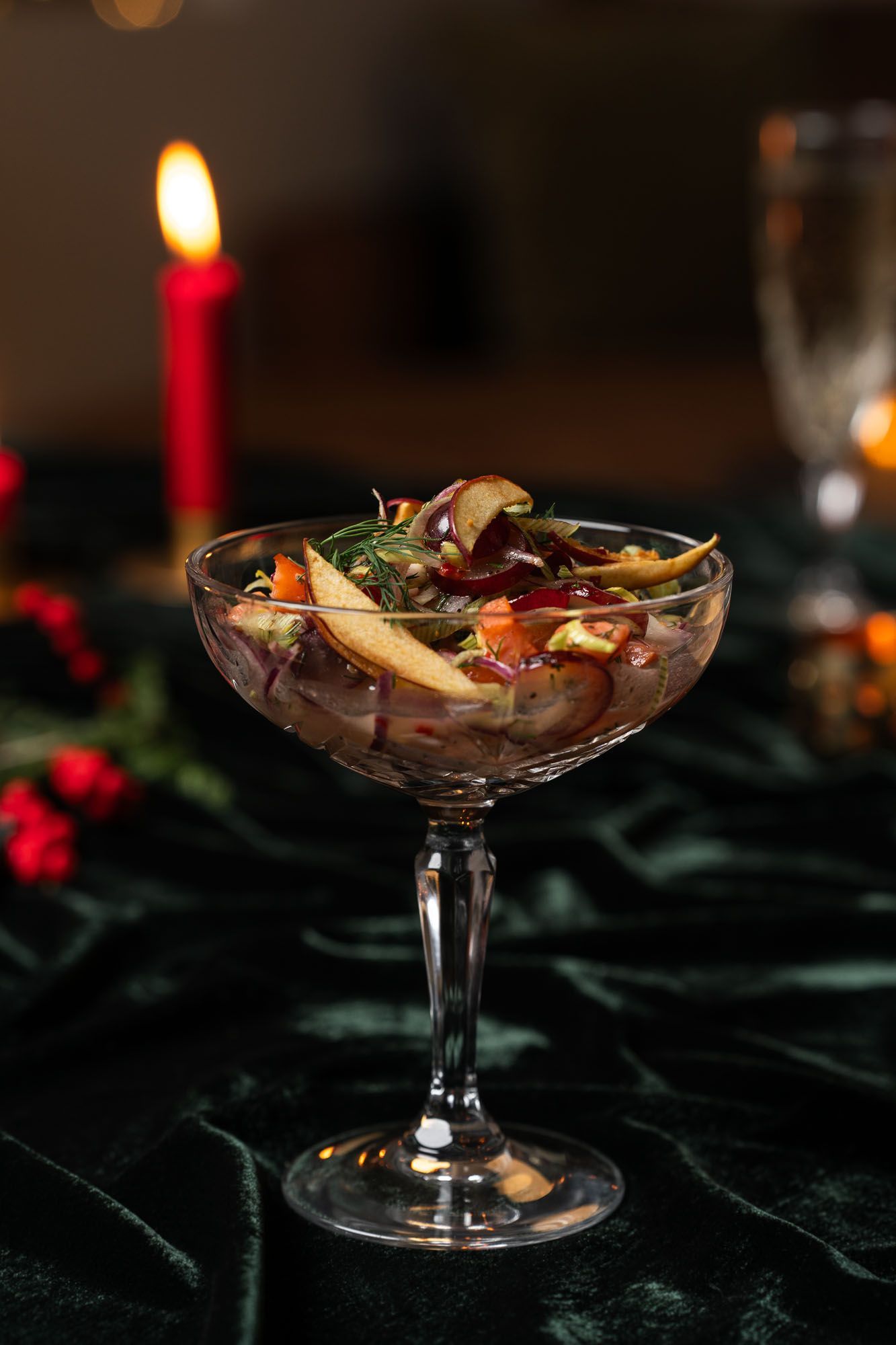 Lítil glerskál með mat, með kveikt kerti í bakgrunni, á dökkgrænum fleti.