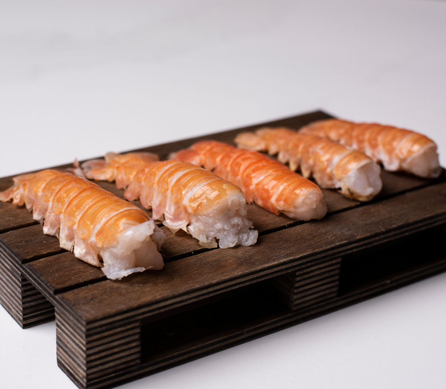 Eldaðir humarhalar á dökkum viðarbretti, settir fram á hvítum fleti.