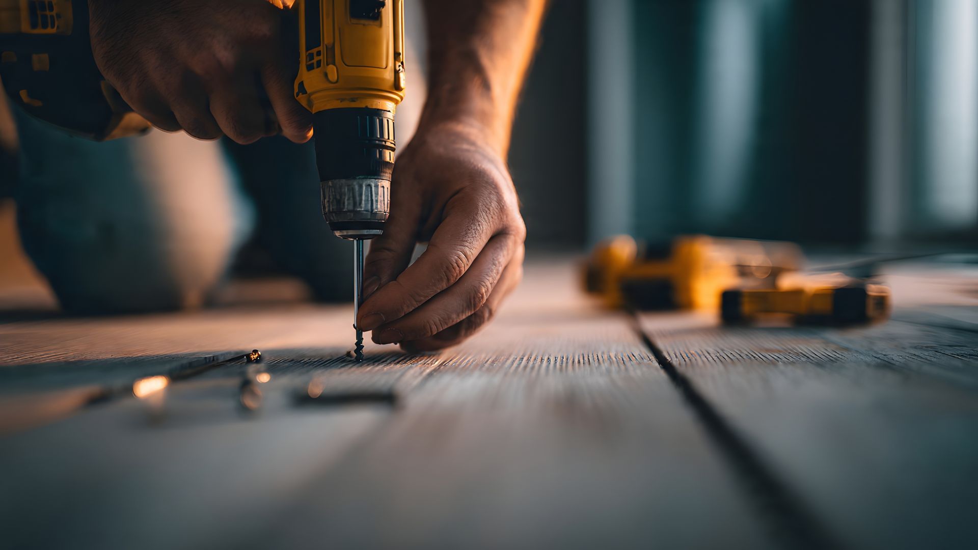Hands using a drill to assemble wood on a workbench, with tools blurred in the background