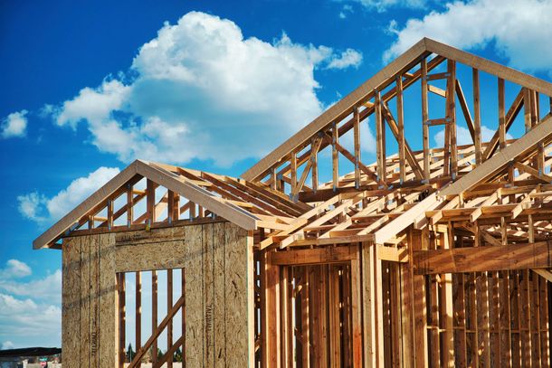 Wood-framed house under construction against a bright blue sky with clouds