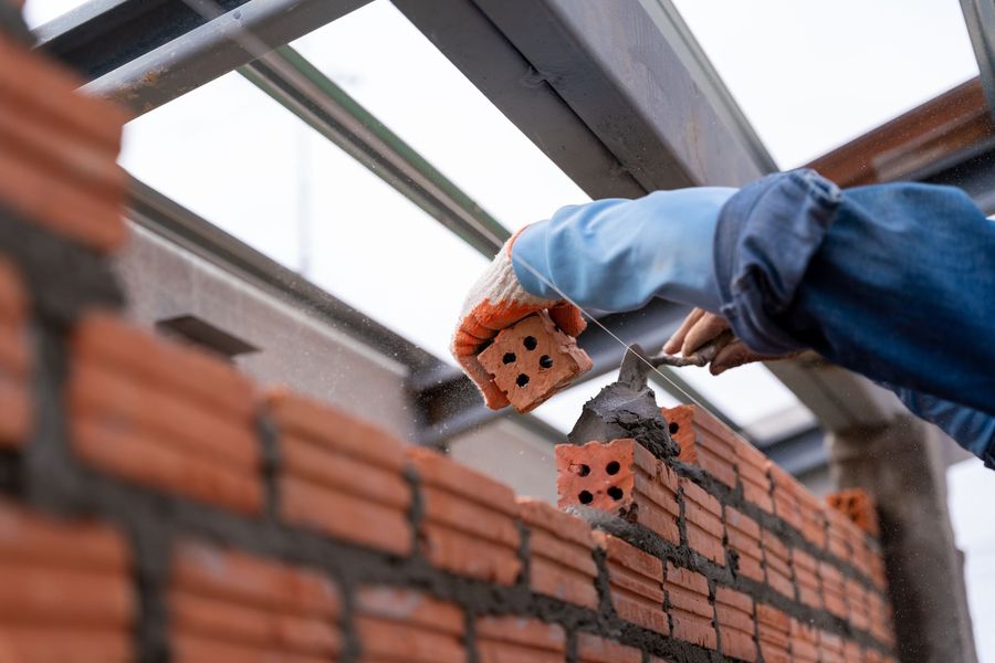 Gloved worker laying red bricks on a wall at a construction site