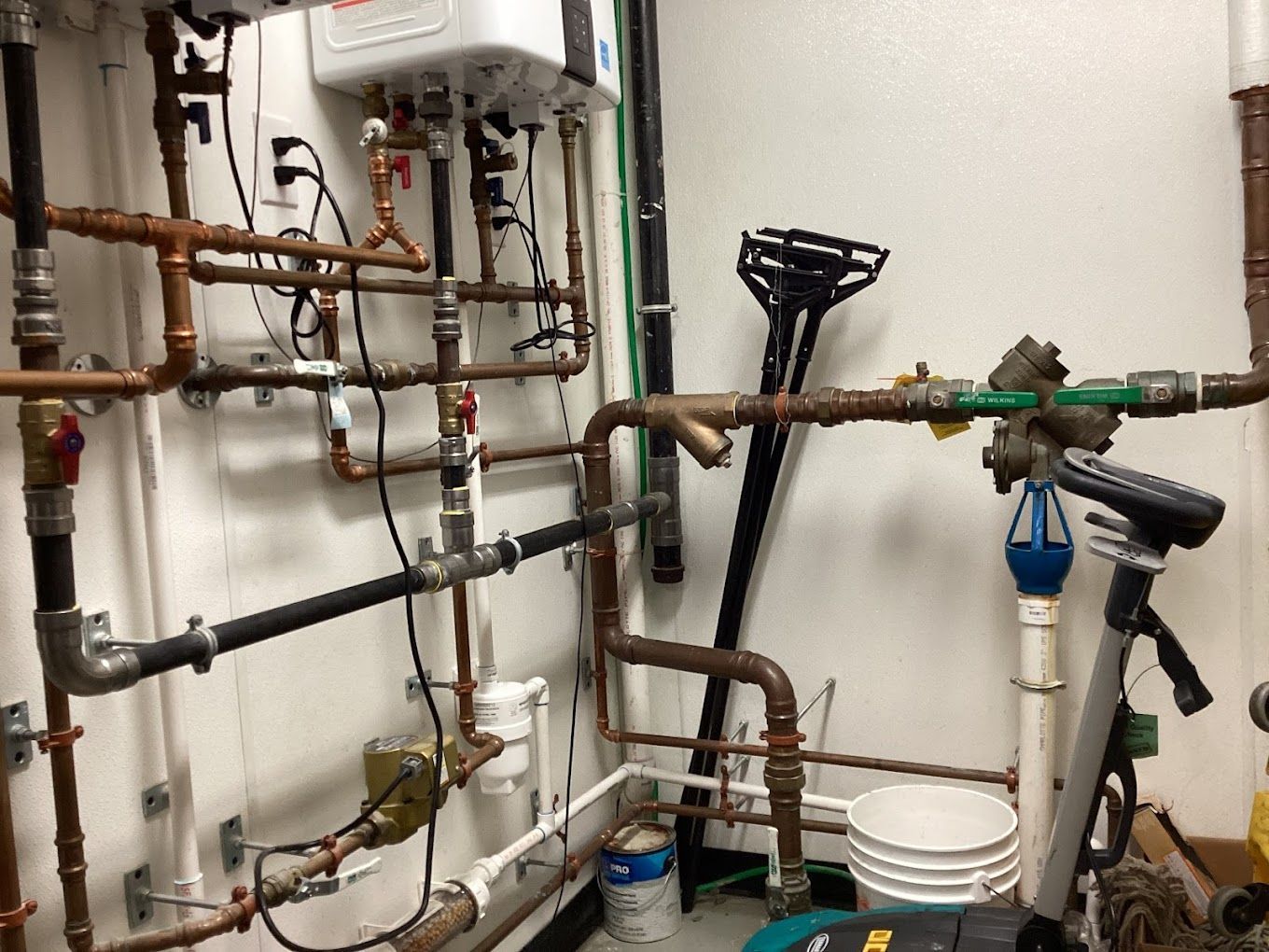 A room with a lot of pipes and a bucket on the floor