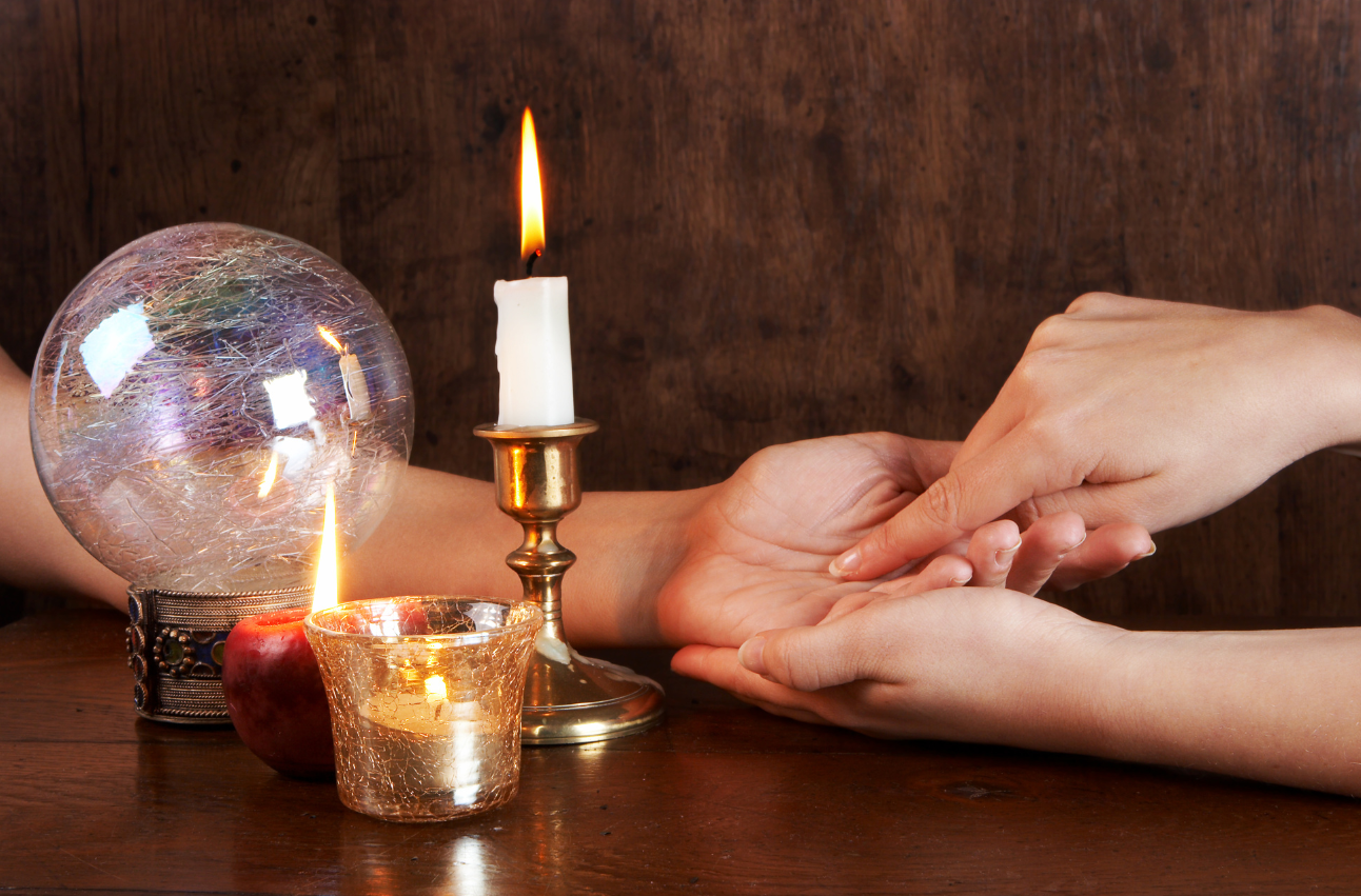 A person is reading someone 's palm with a candle and a crystal ball.