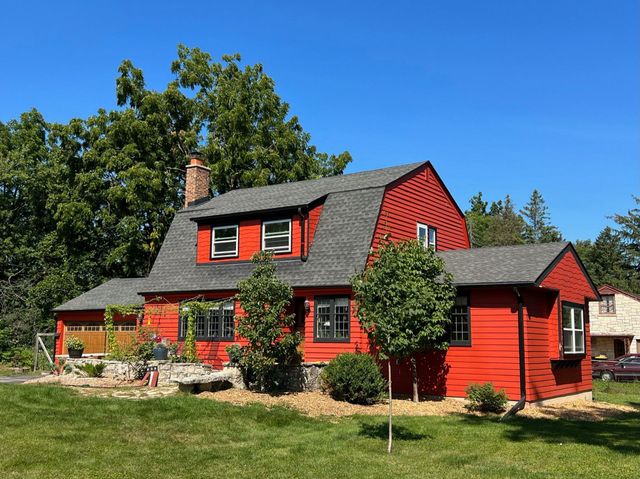 WCL ConstructionPaint Carpentry Inc - A red house with a gray roof sits in the middle of a lush green field.