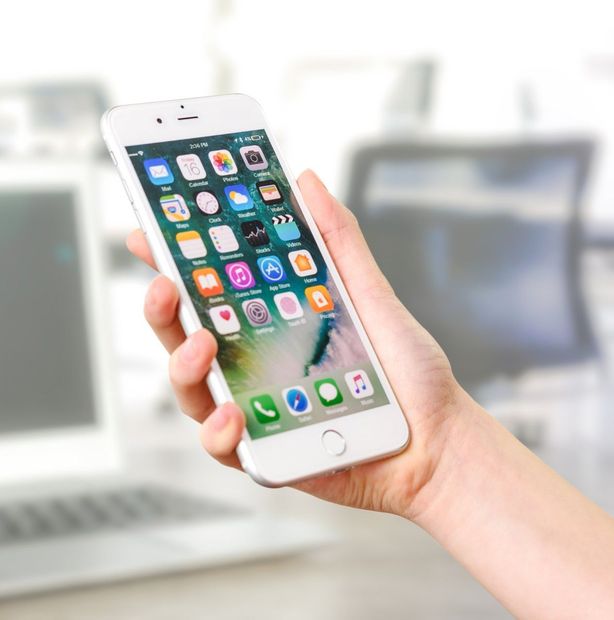 A hand holds up a white iPhone with the home screen open