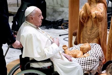 Pope Francis sitting with a wooden baby Jesus who is swaddled in a keffiyeh