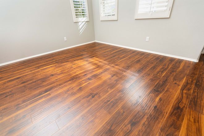 Empty room with glossy dark hardwood floors and light gray walls, lit by daylight from windows. Empty room with glossy dark hardwood floors and light gray walls, lit by daylight from windows.