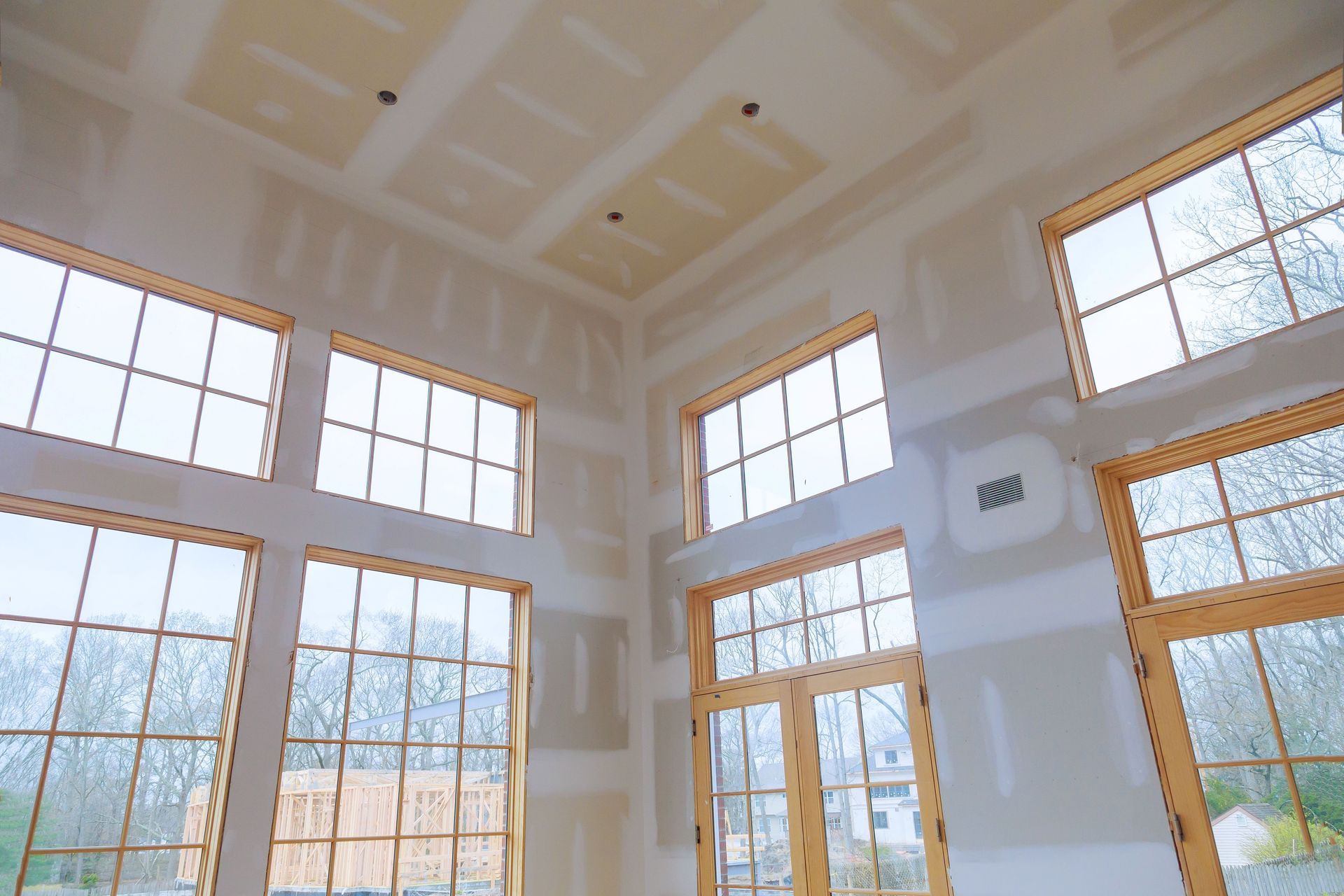Bright sunlit room with large windows and white walls, showing an airy interior and tree branches outside.