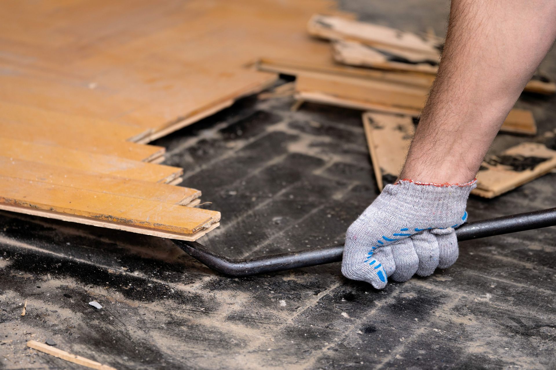Gloved hand prying up old wooden flooring with a crowbar during renovation
