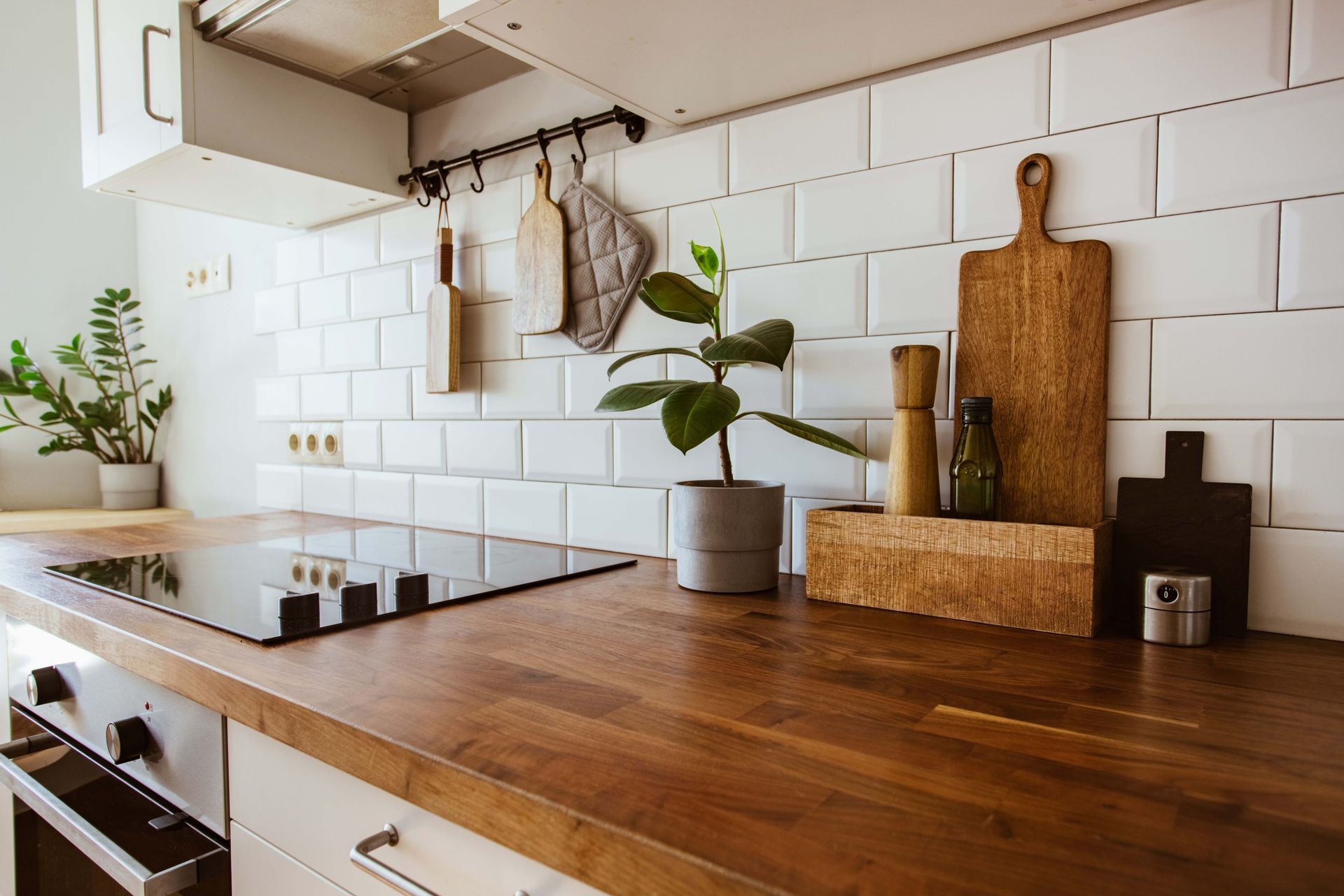 Modern kitchen countertop with wooden cutting boards, white tile backsplash, potted plant, and stove. Modern kitchen countertop with wooden cutting boards, white tile backsplash, potted plant, and stove.