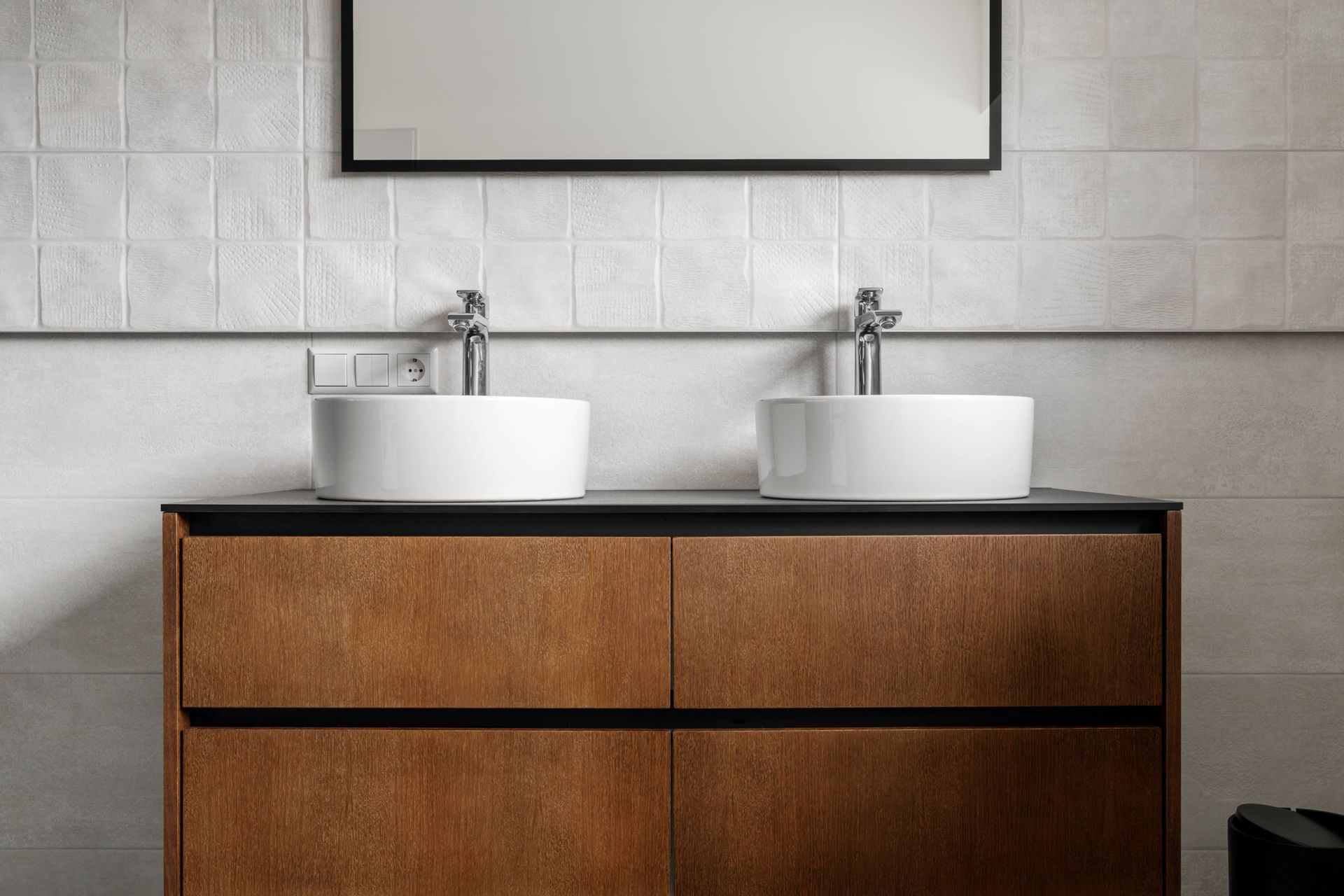 Modern bathroom vanity with two white sinks and chrome faucets against a tiled wall Modern bathroom vanity with two white sinks and chrome faucets against a tiled wall