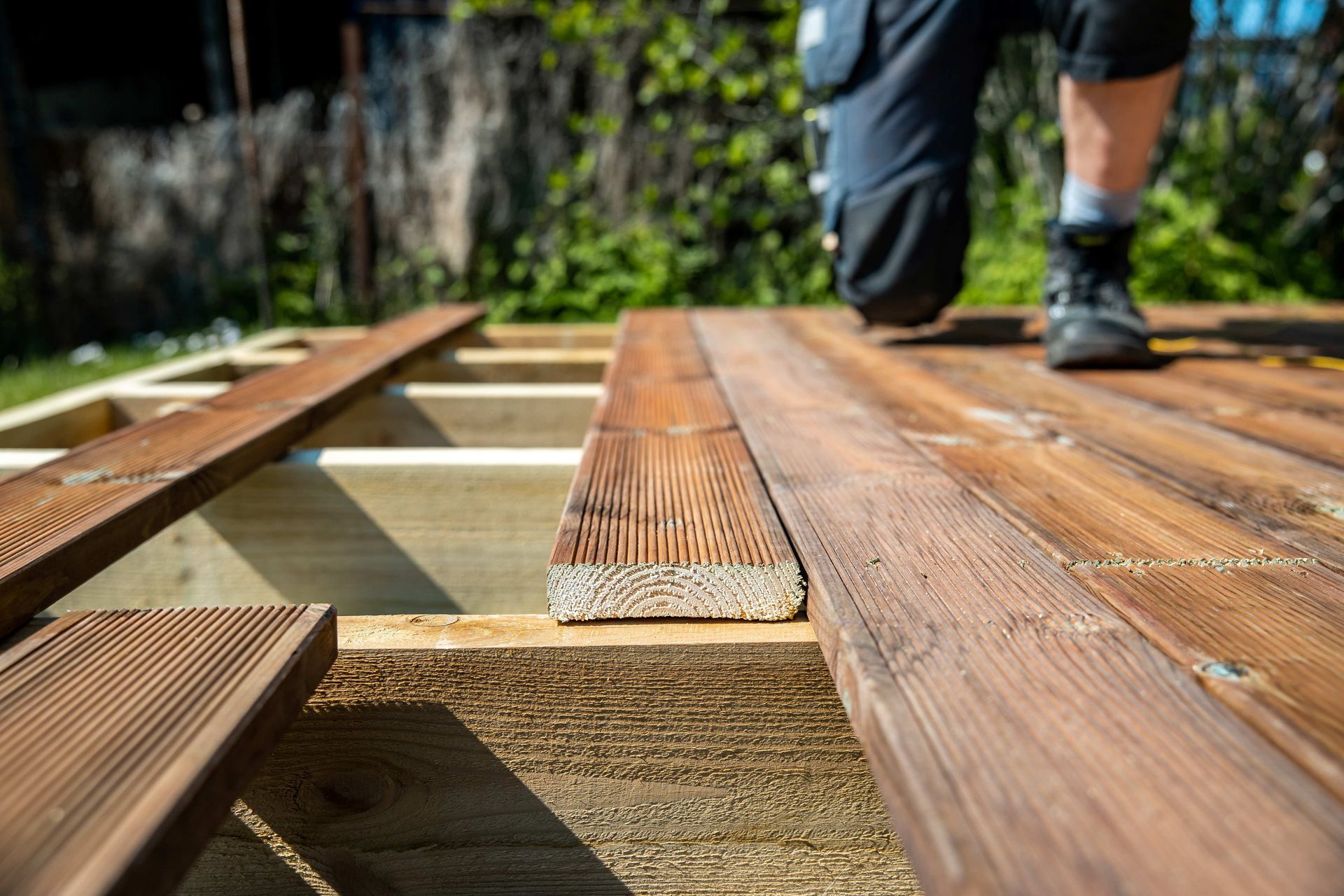 Person installing wooden deck boards outdoors, with tools and framing visible