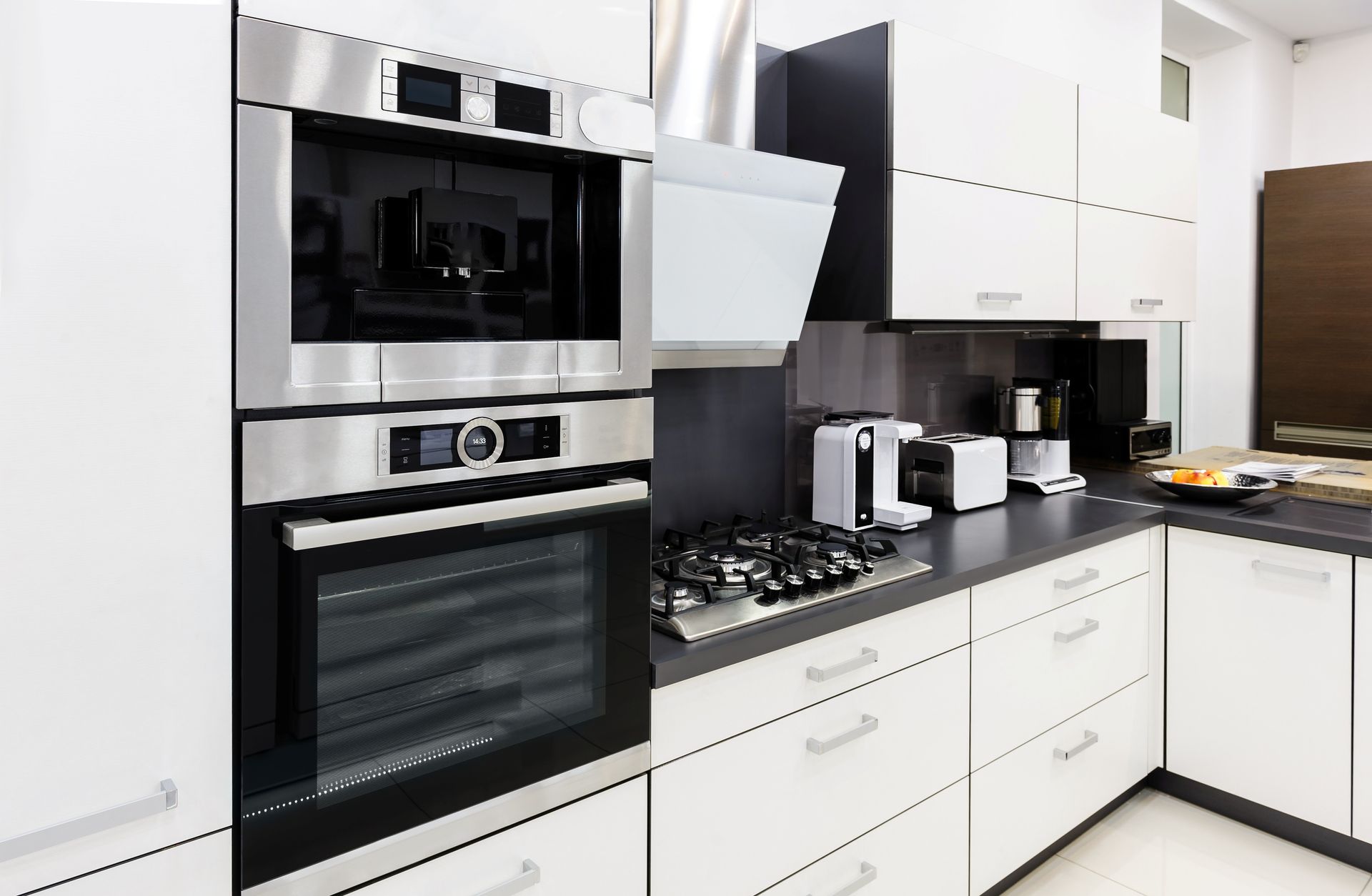Modern white kitchen with built-in stainless steel oven, stovetop, and countertop appliances Modern white kitchen with built-in stainless steel oven, stovetop, and countertop appliances
