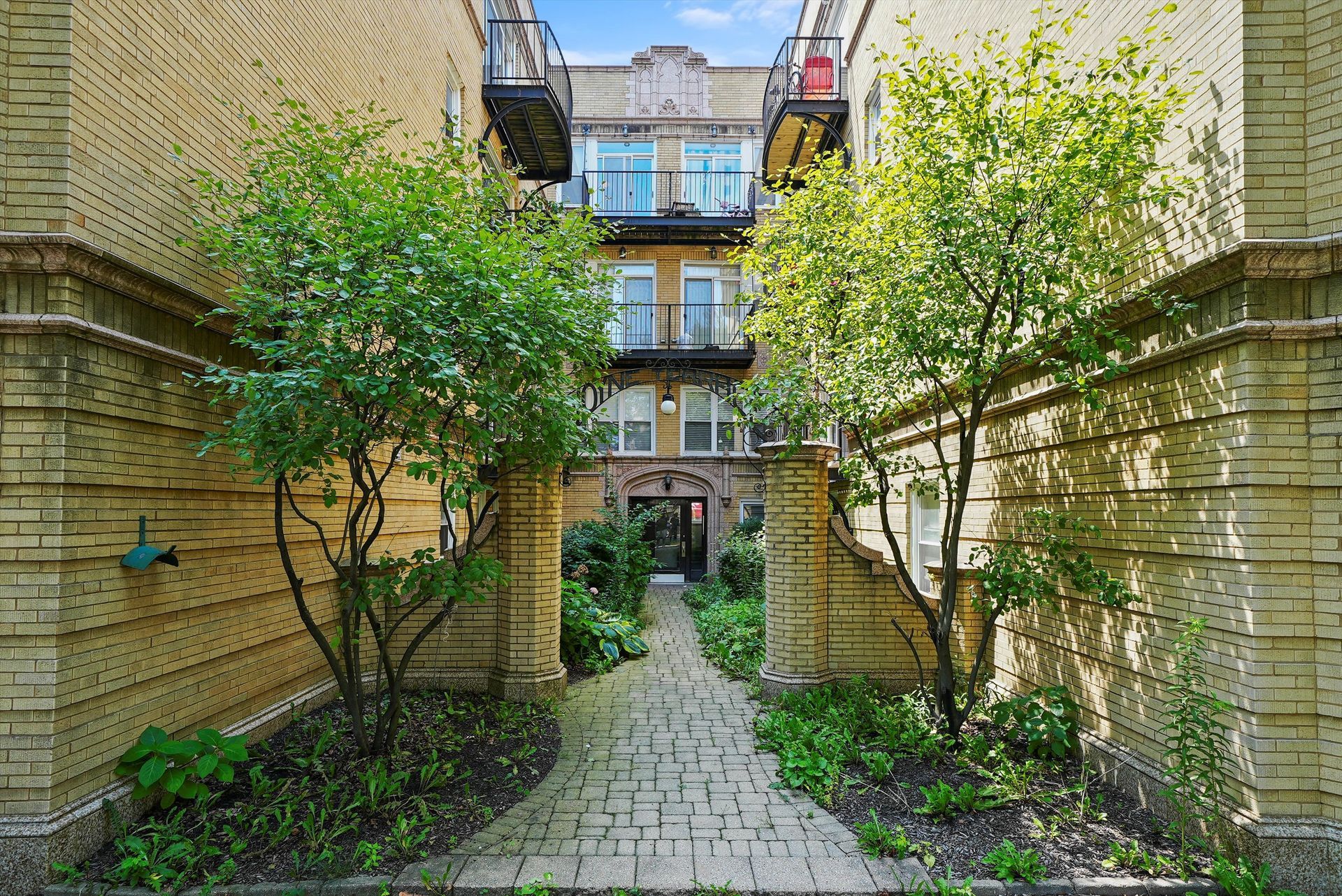 Courtyard entrance with brick path, greenery, and ornate building facade.