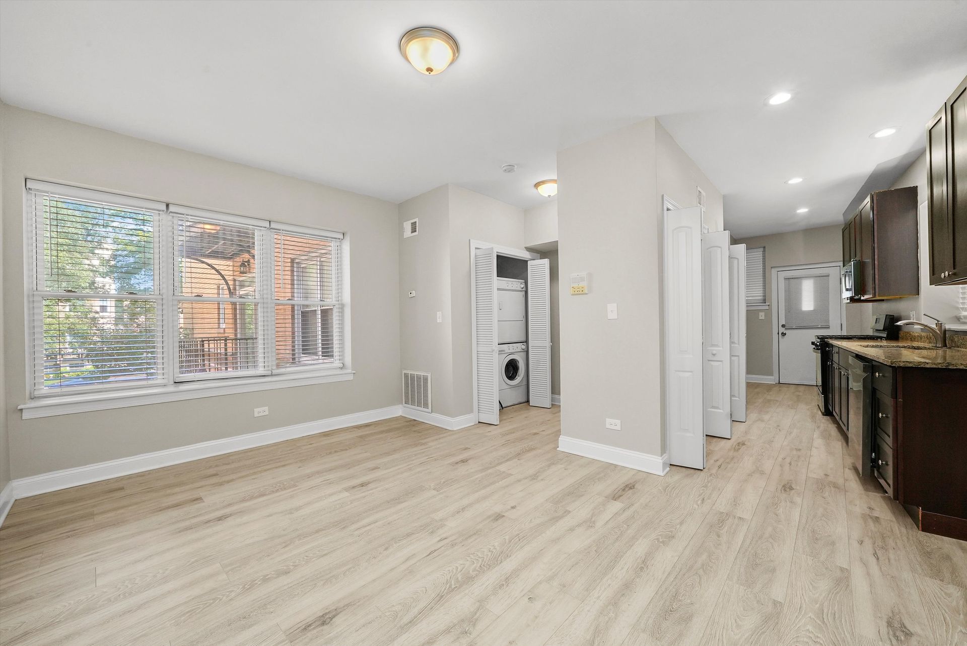 Bright, modern apartment interior with light wood floors, large windows, and a kitchen.