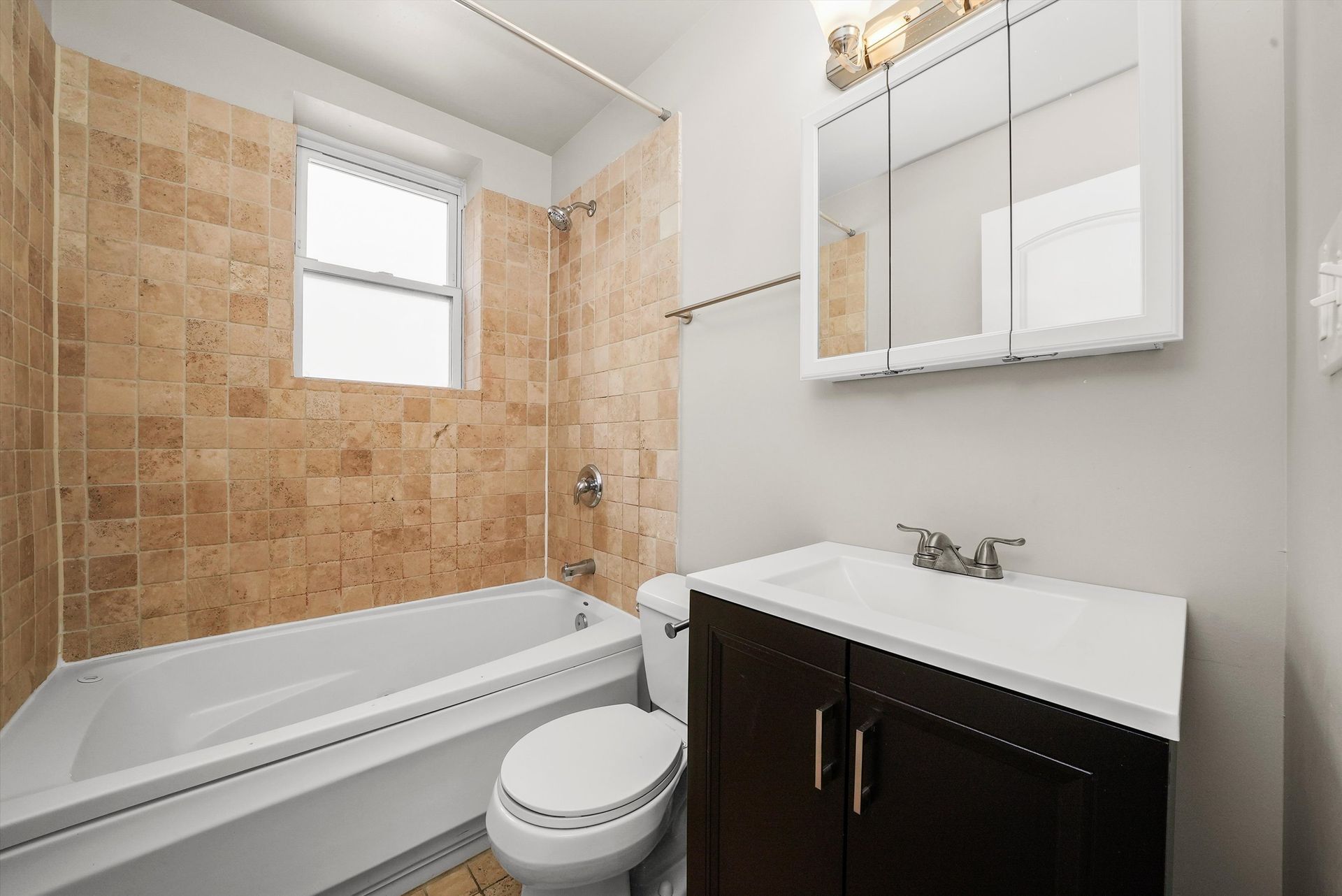 Bathroom with brown tile, white fixtures, and dark vanity.