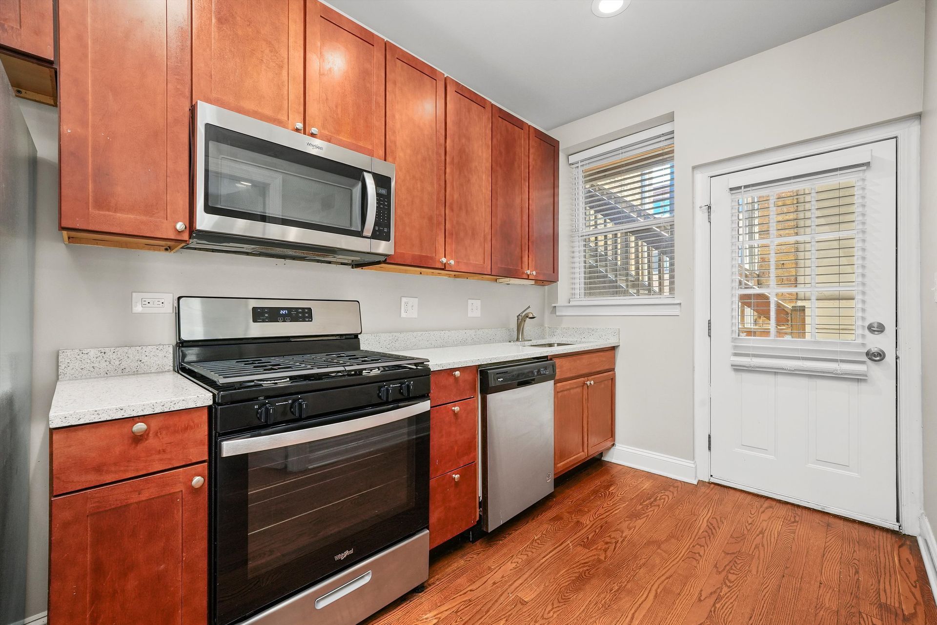 A kitchen with reddish-brown cabinets, stainless steel appliances, and a white countertop.