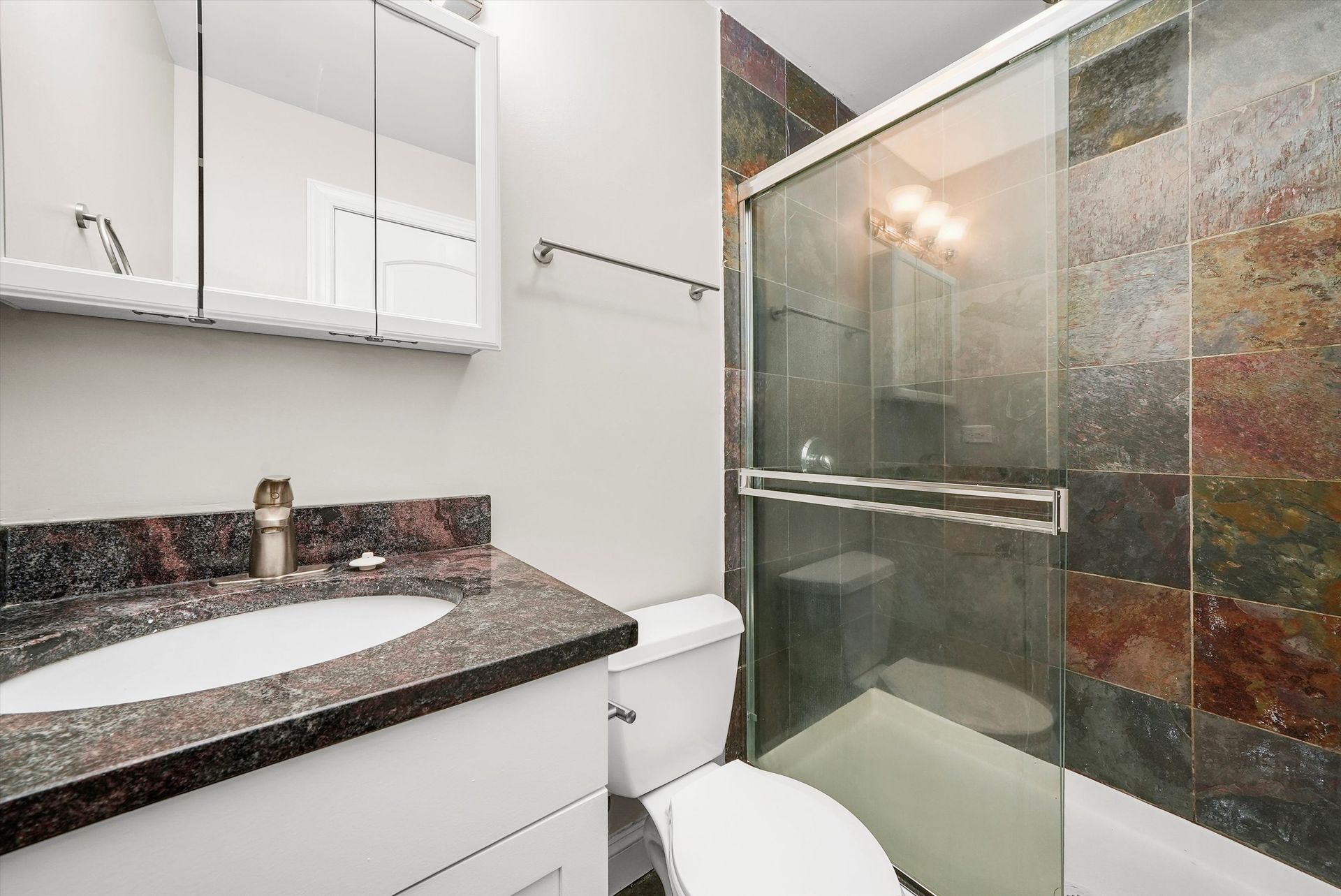 Bathroom with white vanity, toilet, and shower with colorful tile wall.