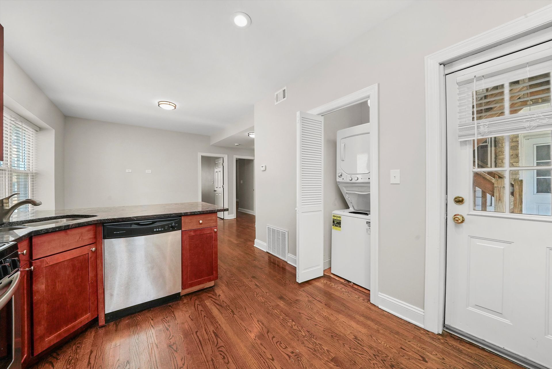 Kitchen with red cabinets, stainless steel appliances, wooden floor, and a door leading outside.