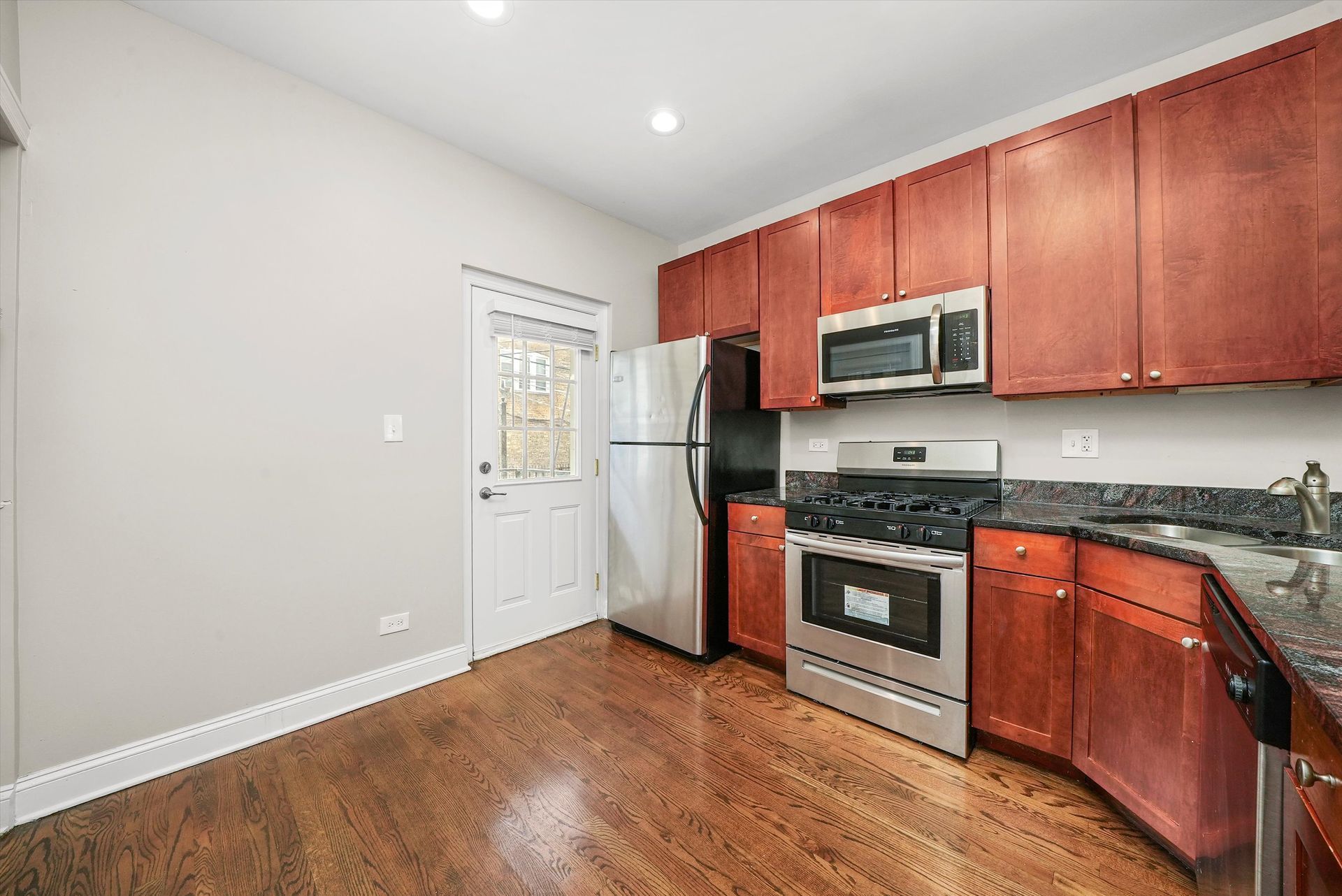 A kitchen with wood cabinets, stainless steel appliances, and a door to the outside.