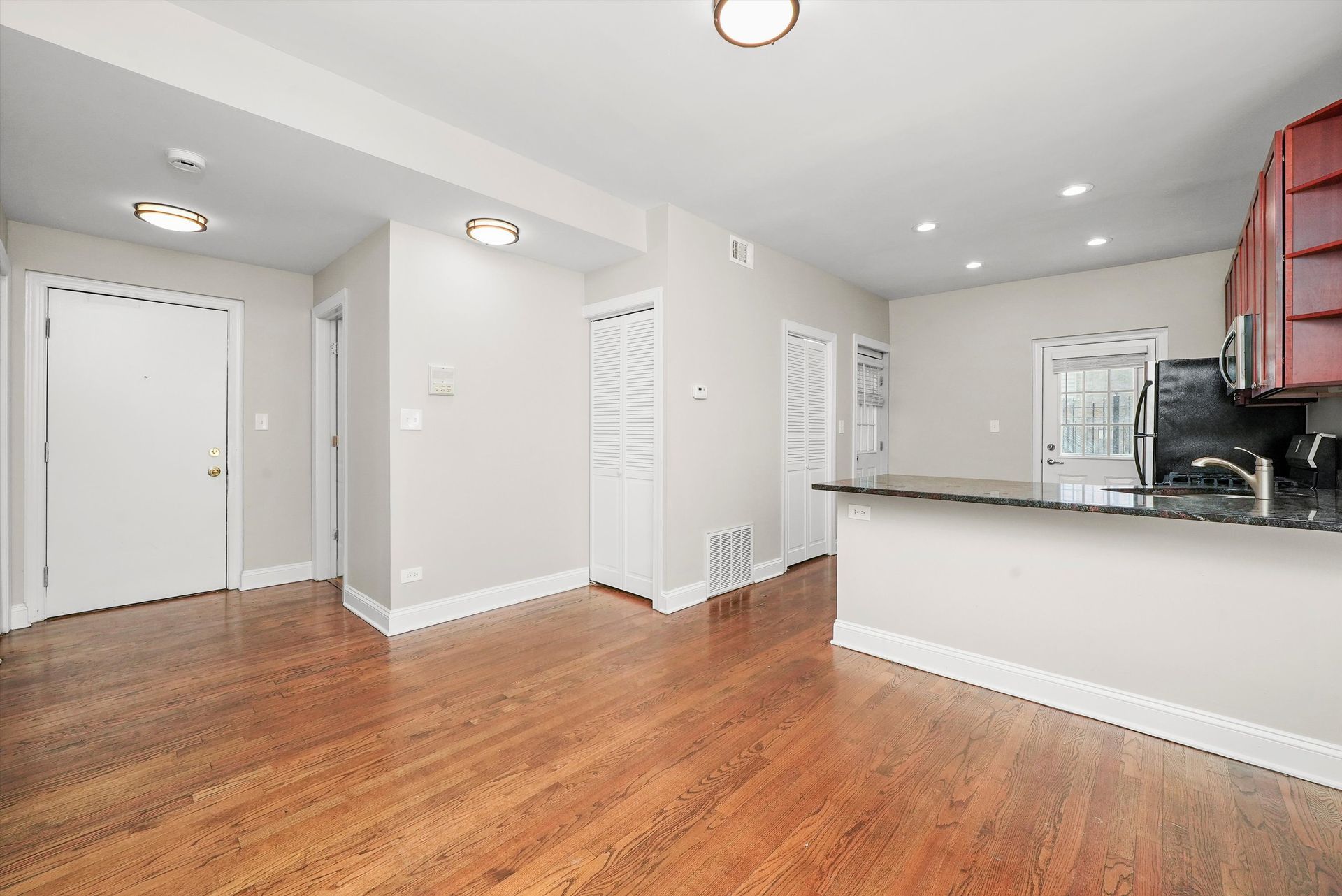 Empty apartment interior with hardwood floors, white walls, and a kitchen.