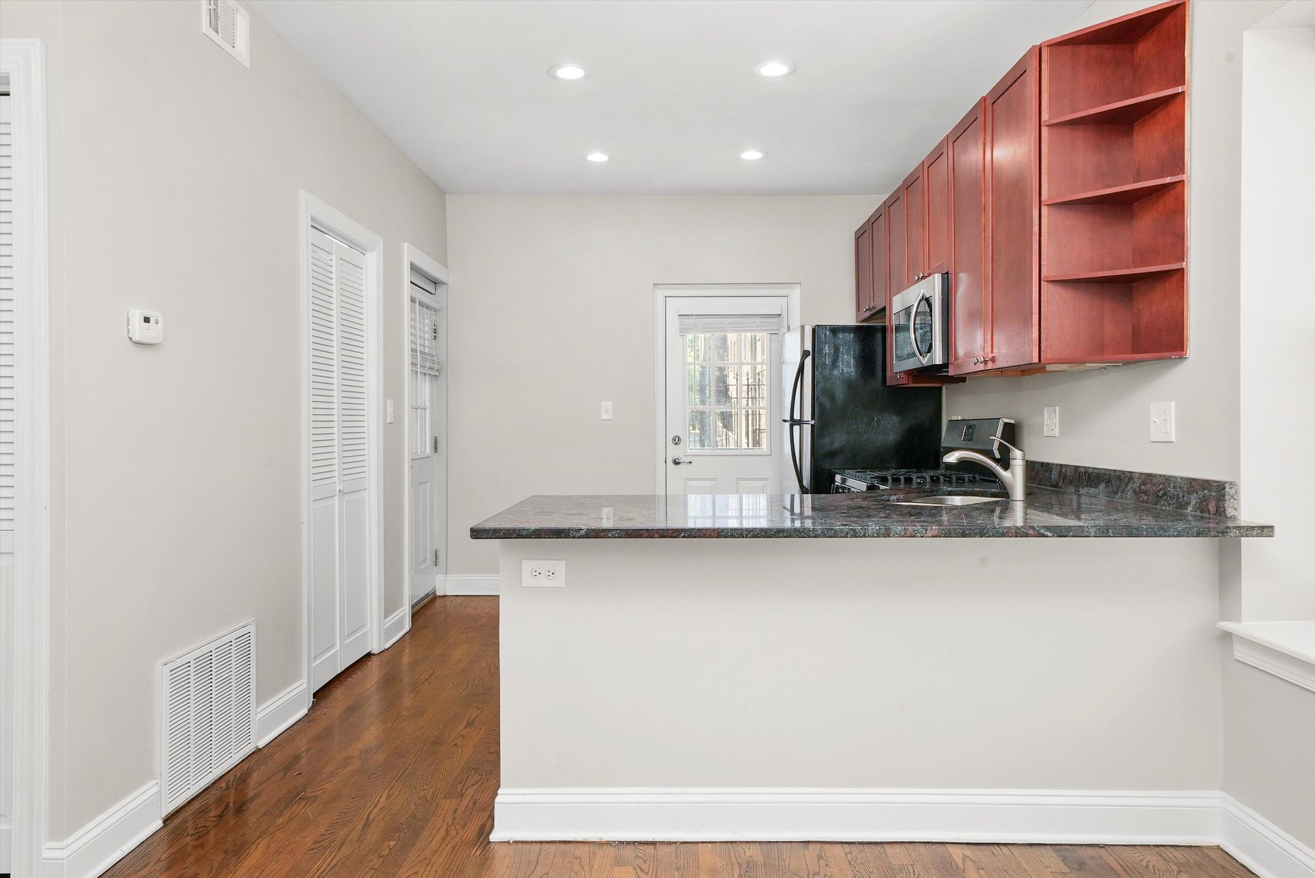 Kitchen with red cabinets, dark countertops, and a door to the outside.