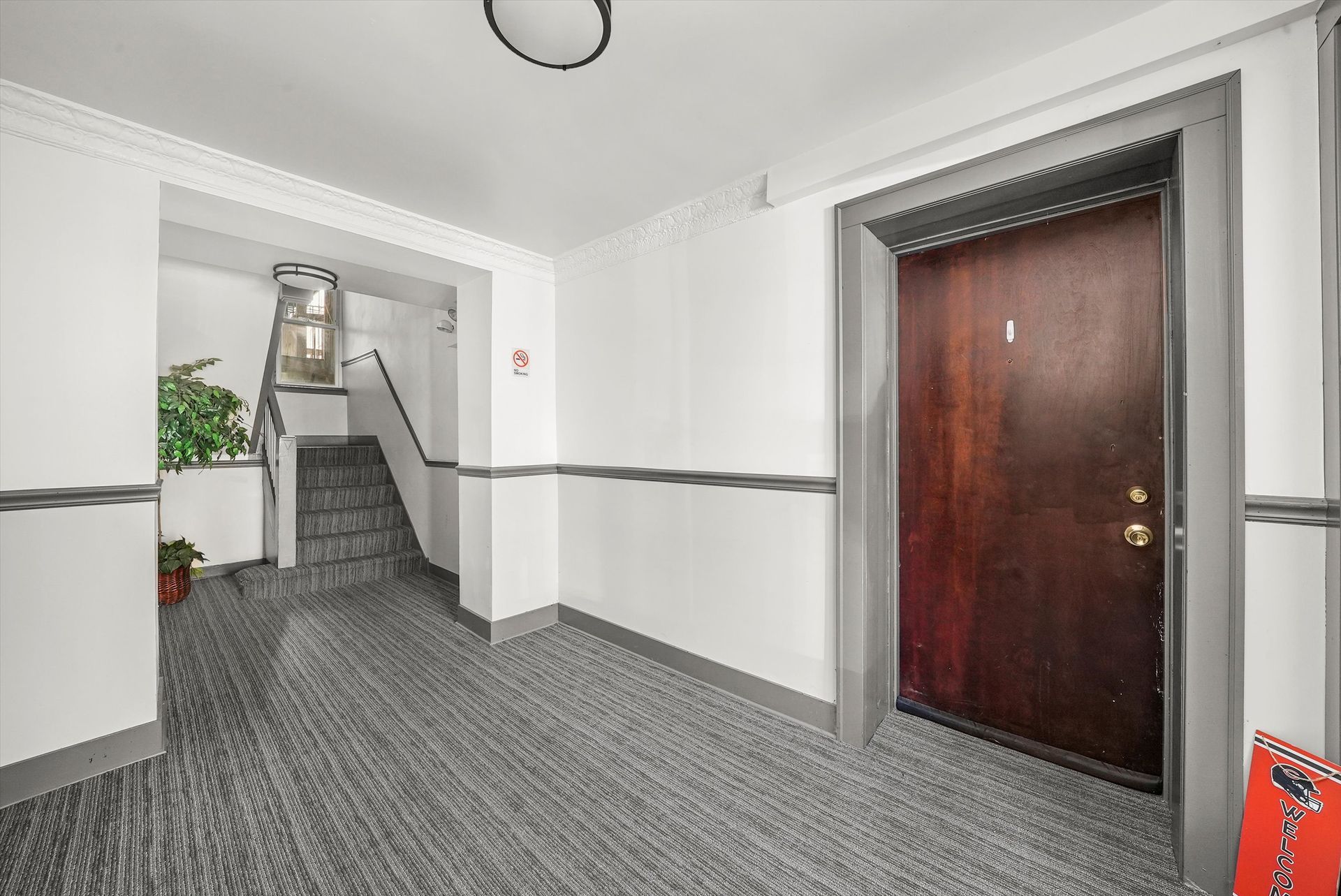 Apartment hallway with dark wood door, staircase, and patterned gray carpet.