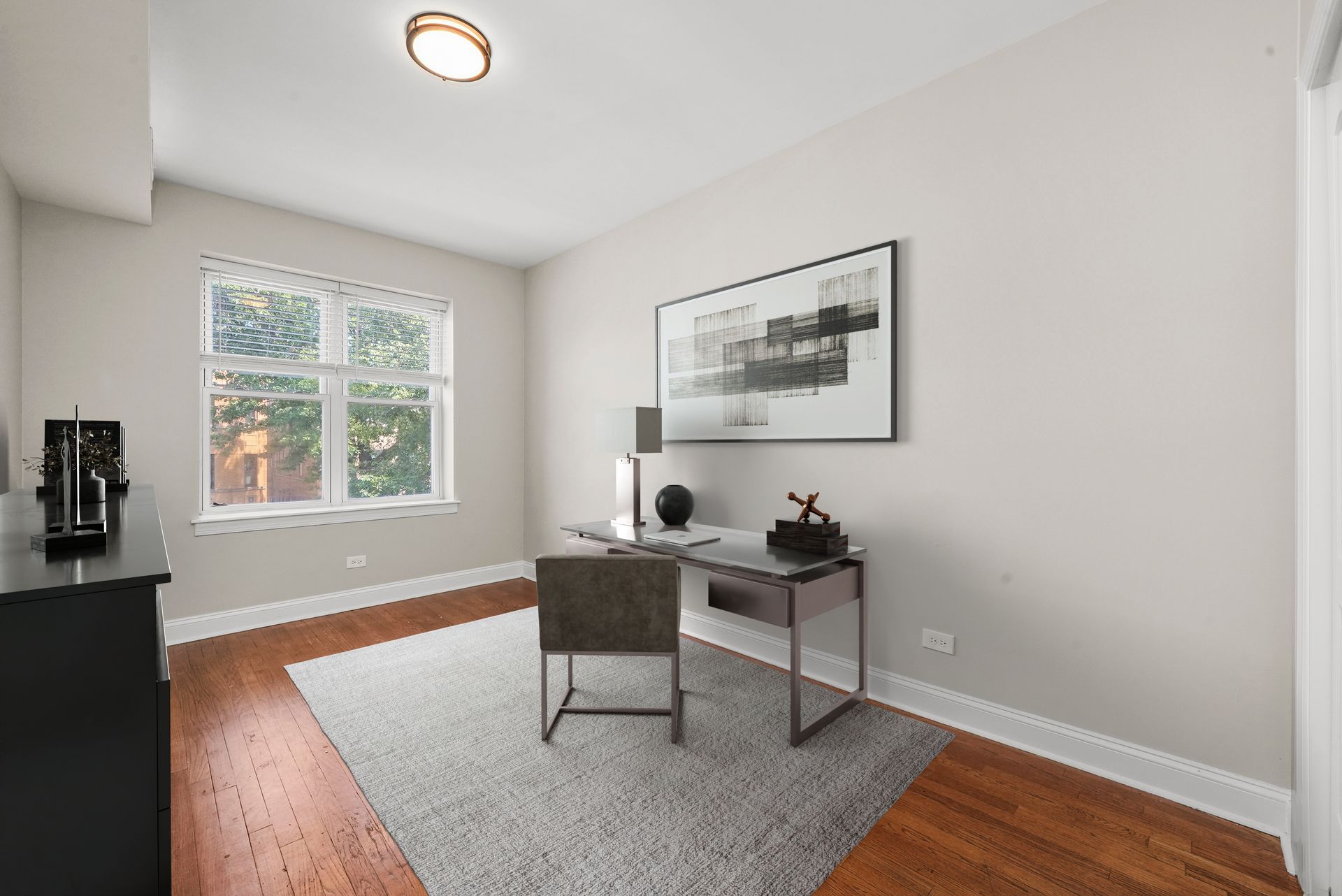 Home office with desk, artwork, window, and rug; neutral color palette.