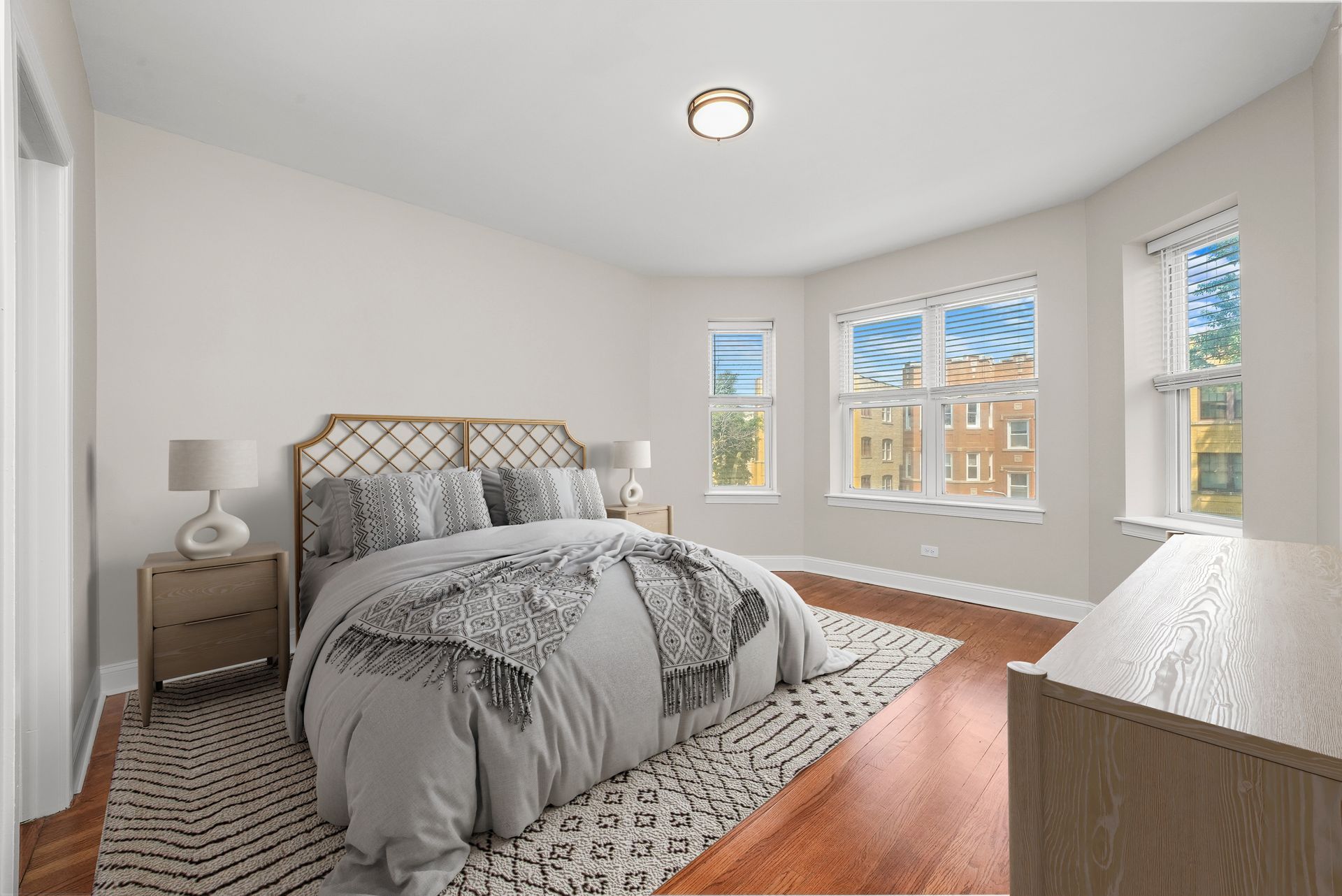 Bedroom with bed, nightstands, windows, and dresser; hardwood floors, neutral color palette.