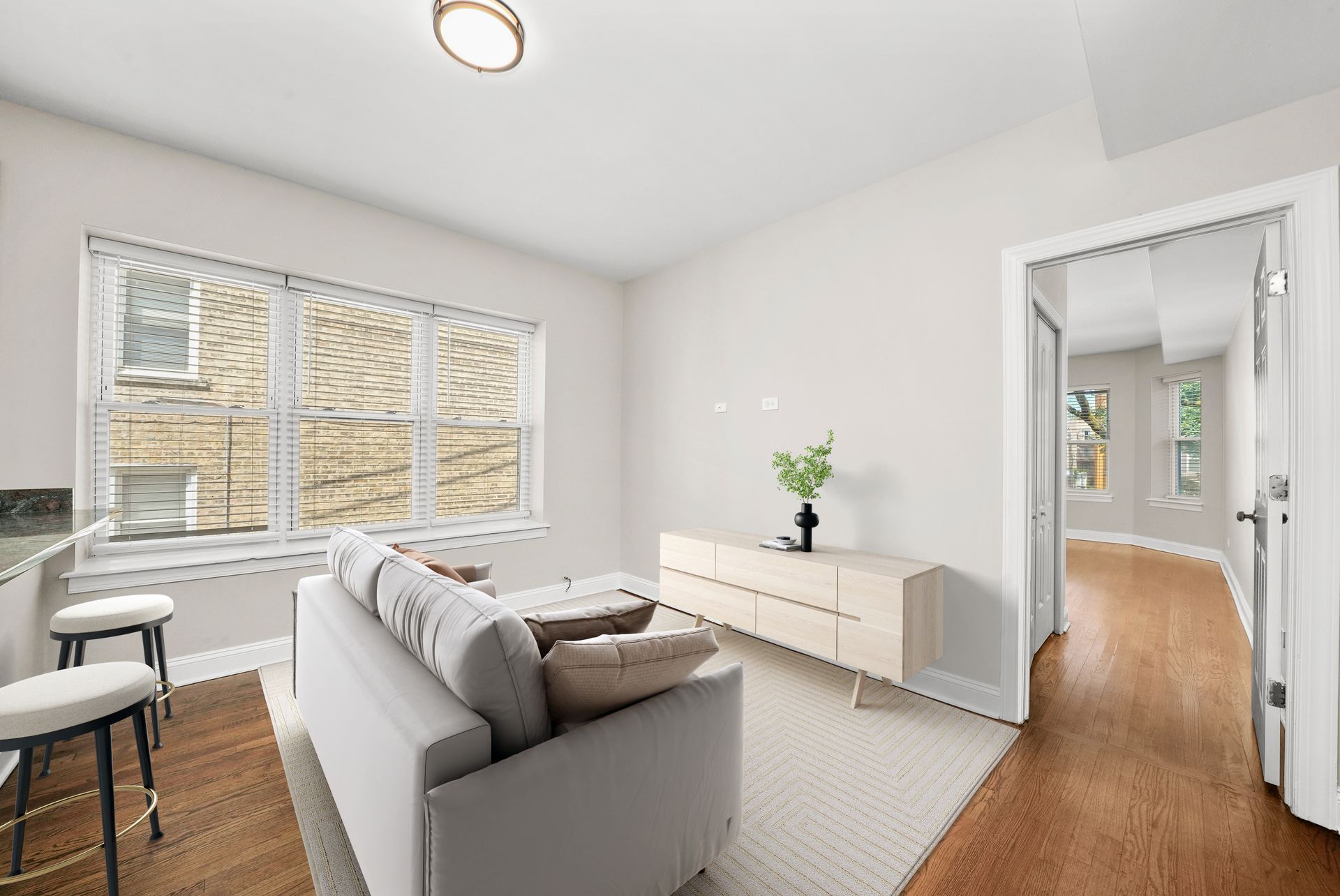 Living room with sofa, windows, hardwood floors, and open doorway to hallway.