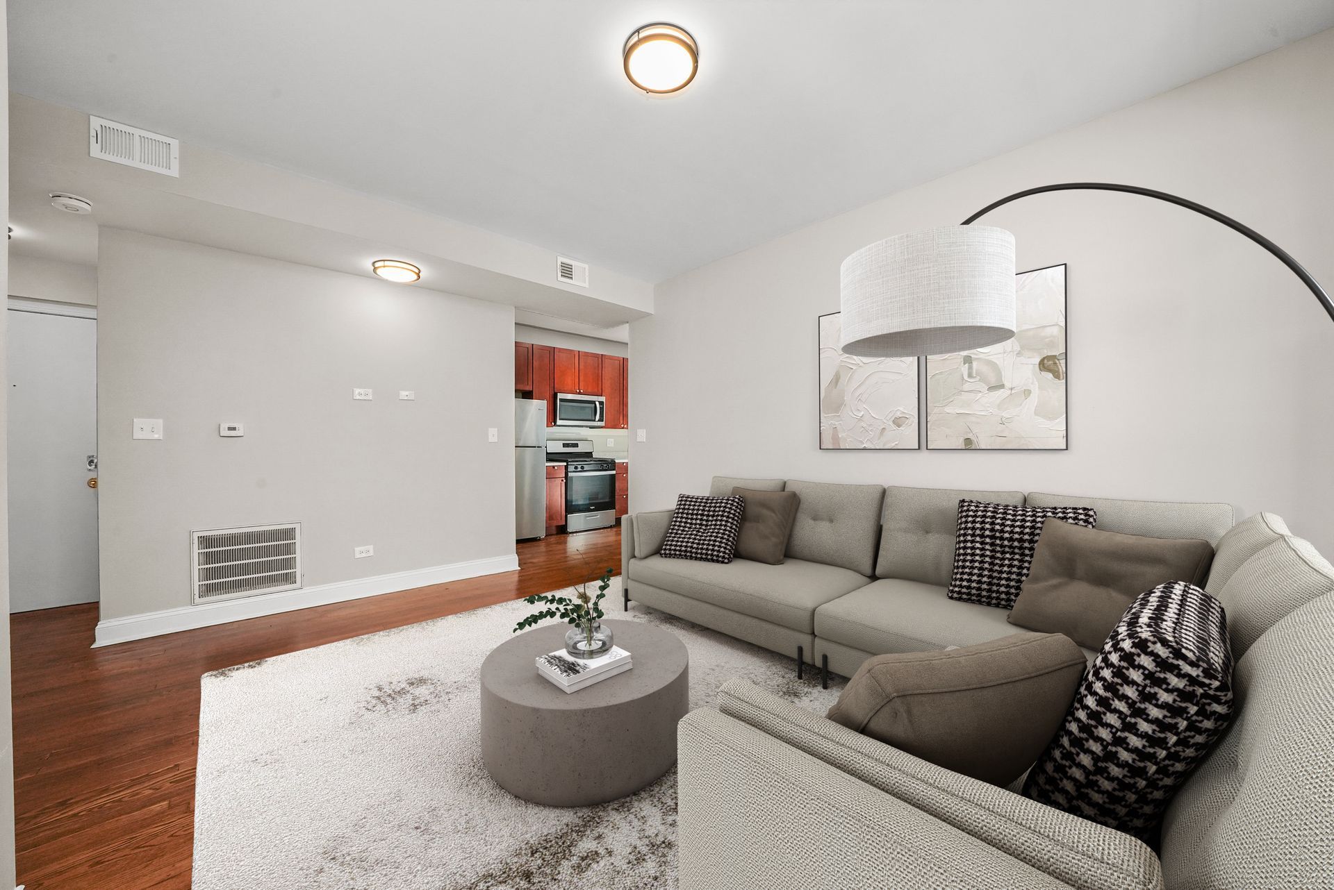 Living room with gray sofa, rug, round coffee table, and small kitchen in the background.