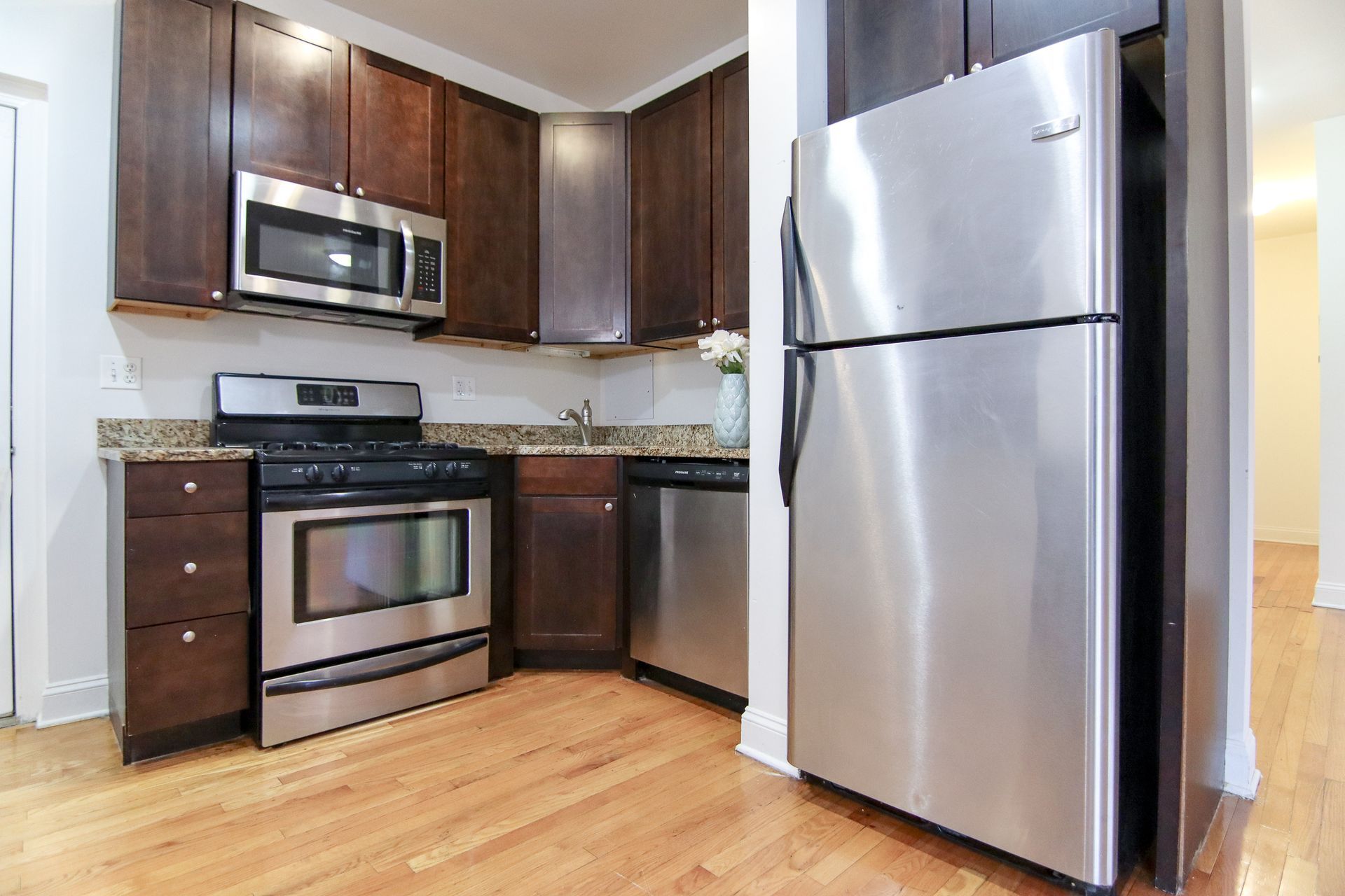 Stainless steel kitchen with wooden cabinets and a light wood floor.