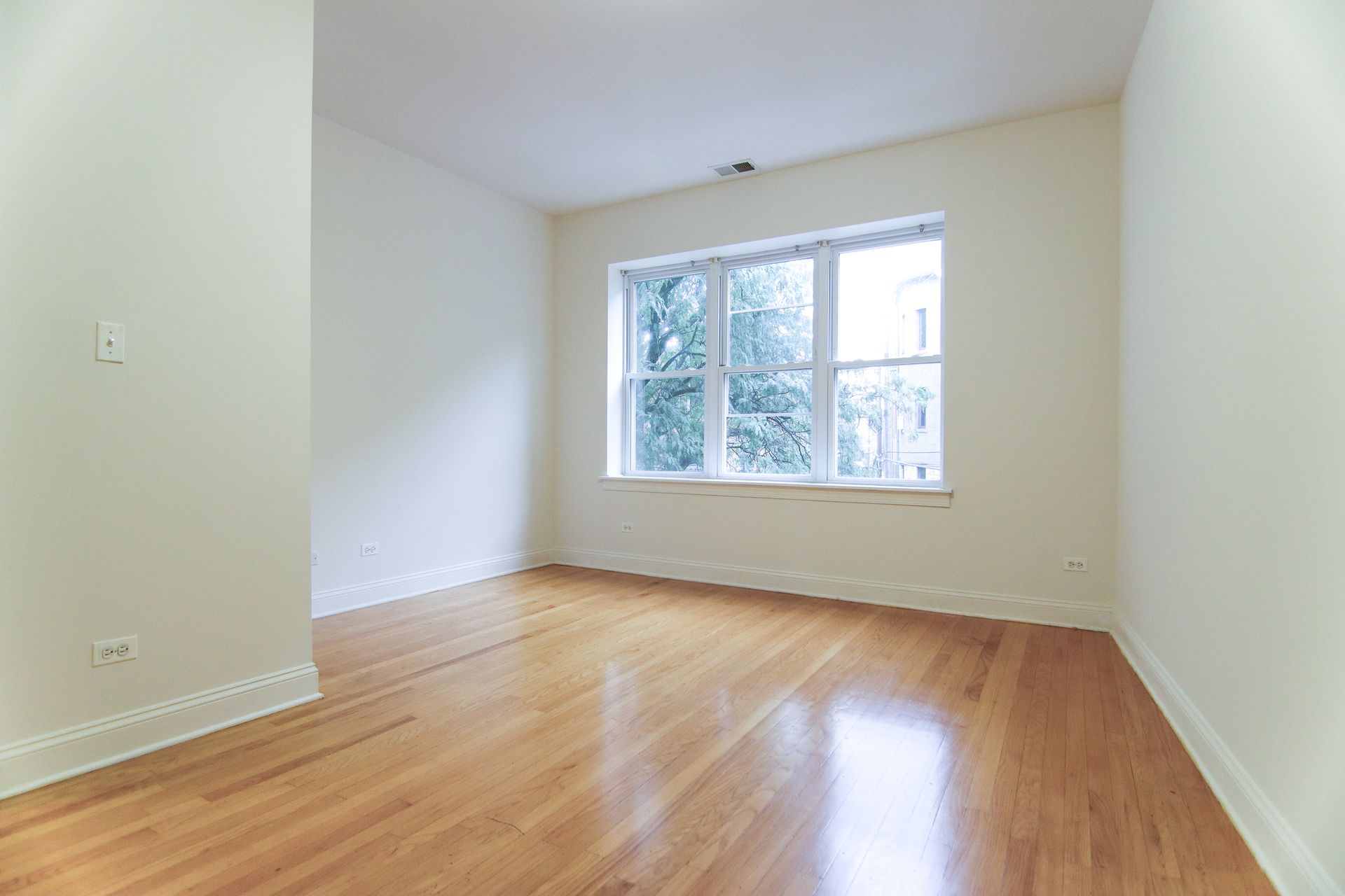 Empty room with hardwood floors, a window, and white walls.