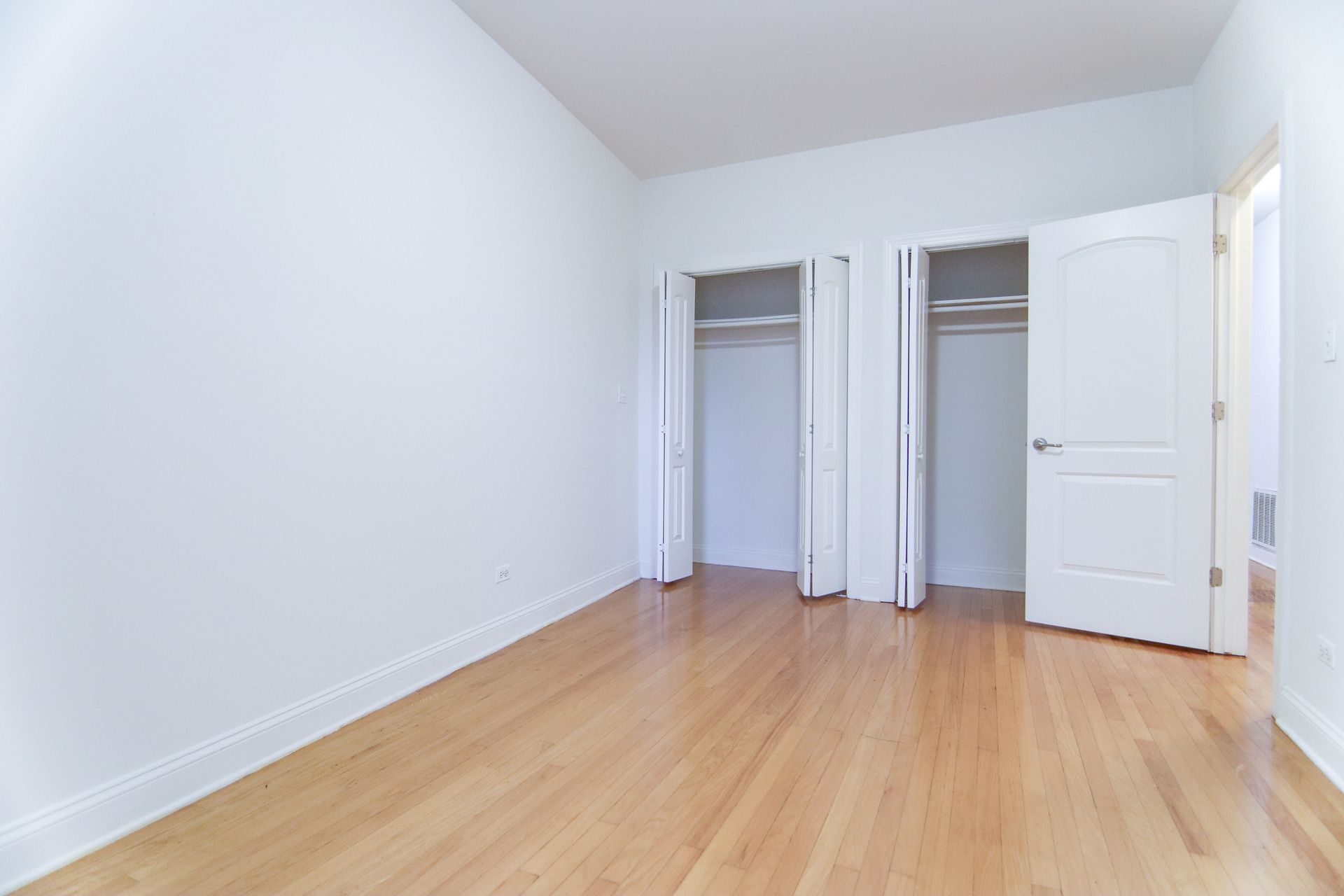 Empty room with wood floor, white walls, two closets, and an open door.