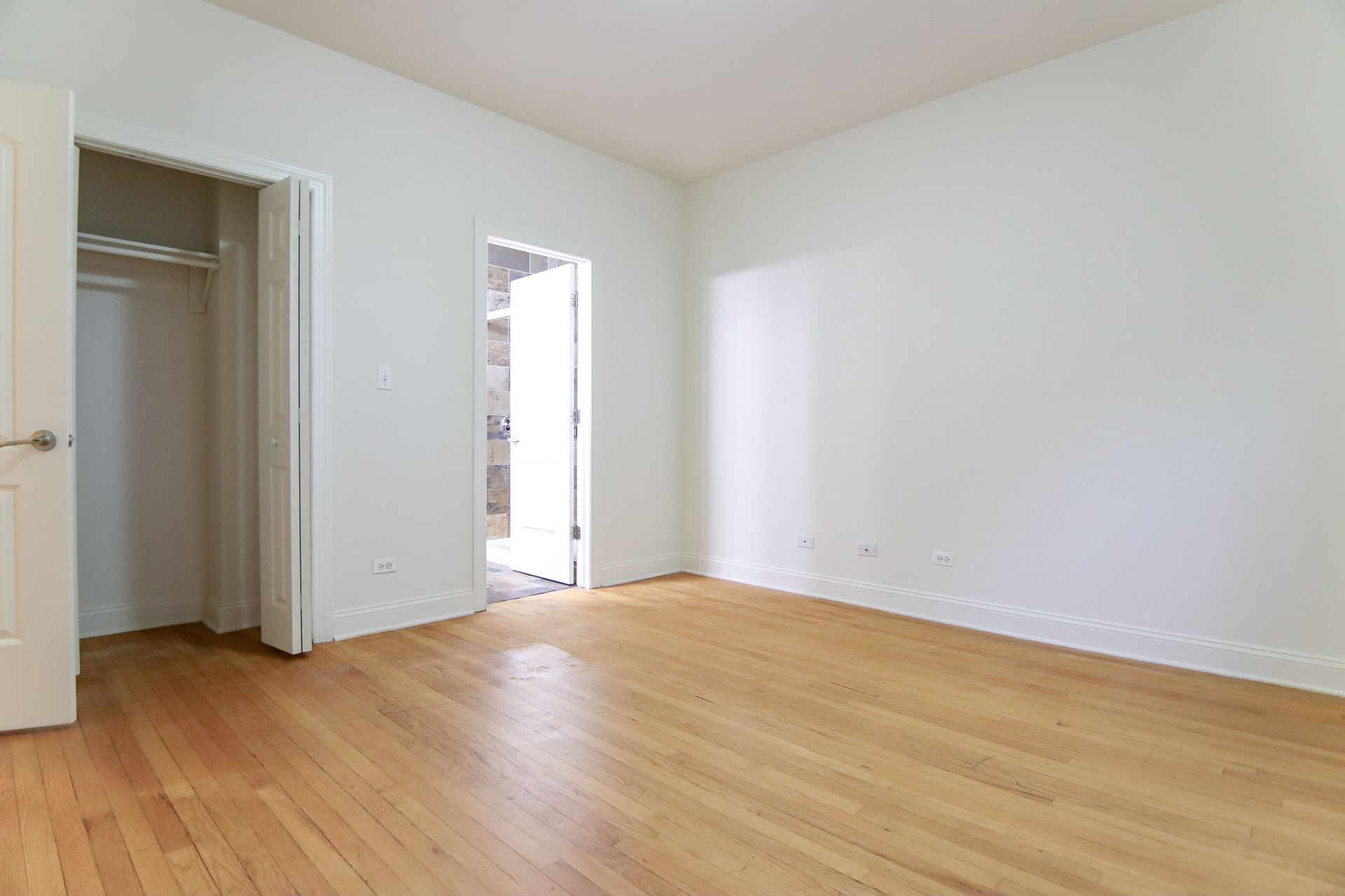 Empty room with hardwood floors, white walls, closet, and open doorway.