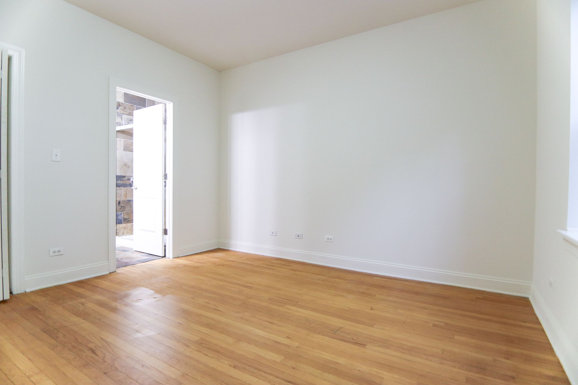 Empty room with hardwood floors, white walls, and an open doorway.