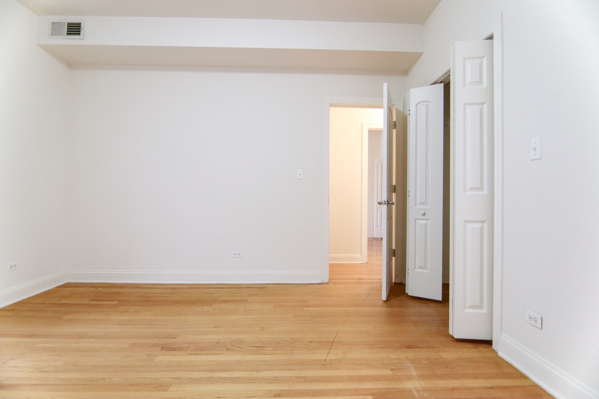 Empty room with hardwood floors and white walls.  Two doors open to hallway and closet.