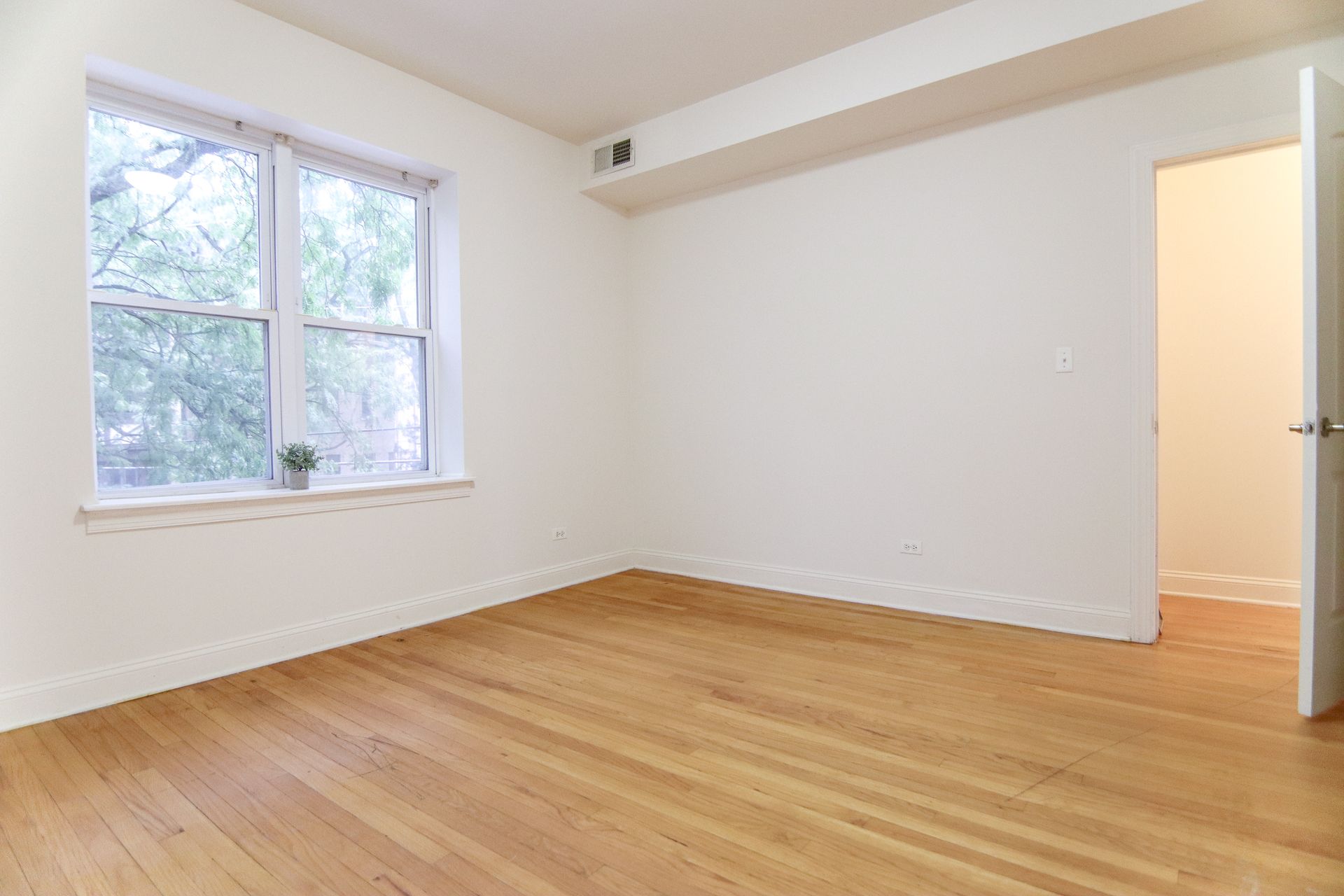 Empty room with hardwood floors, window, and open doorway.
