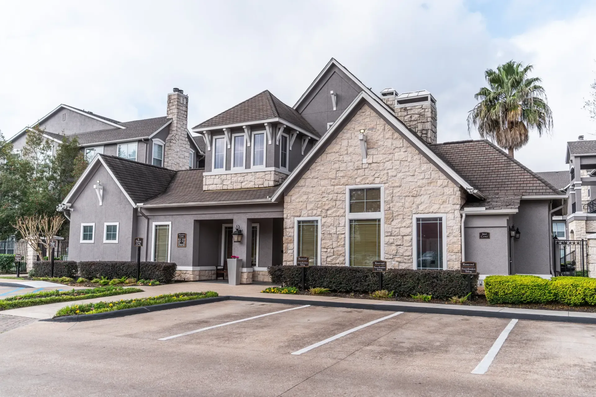 Westpark Ranch Apartments in Houston, TX. A stone building with parking spaces and a palm tree under a cloudy sky.