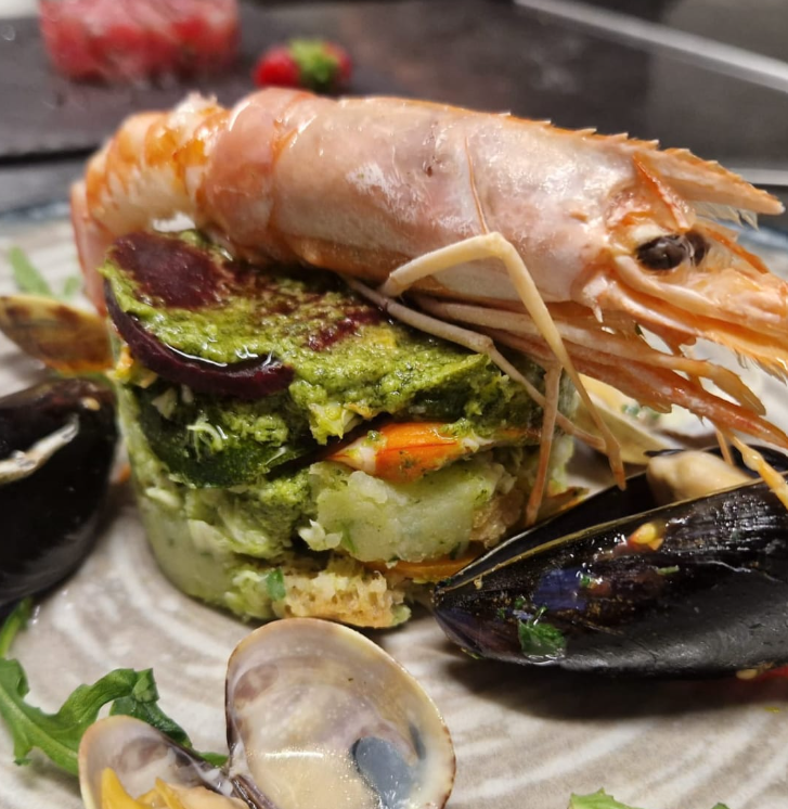 Piatto di frutti di mare: gamberi su una pila di verdure a strati con cozze e vongole sul piatto.