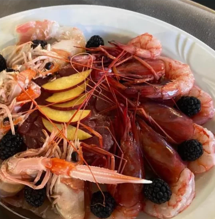 Piatto di pesce fresco, tra cui gamberi, guarnito con frutta e more.