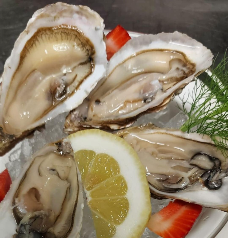 Ostriche su un piatto con limone, fragole ed erbe aromatiche.