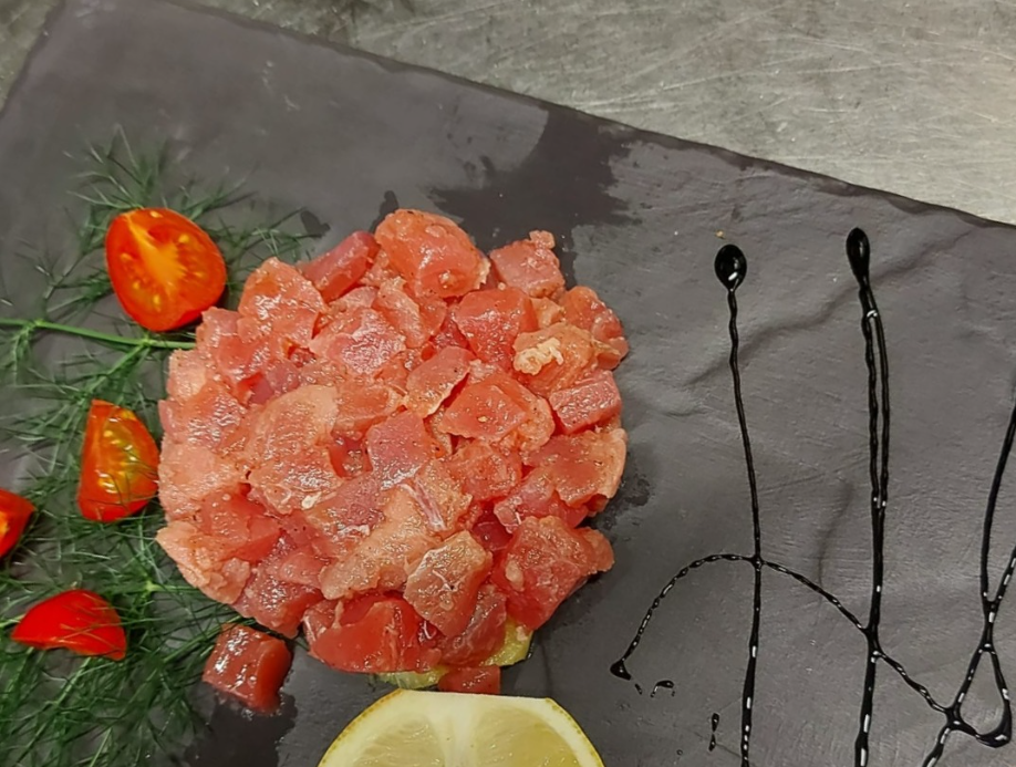 Tartare di tonno su piatto di ardesia nera, guarnita con pomodori, aneto, limone e glassa balsamica.