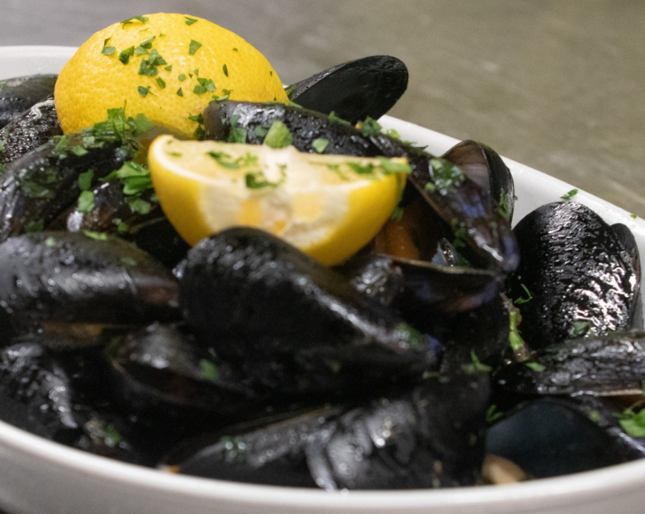 Cozze al vapore in una ciotola bianca, guarnite con limone e prezzemolo.