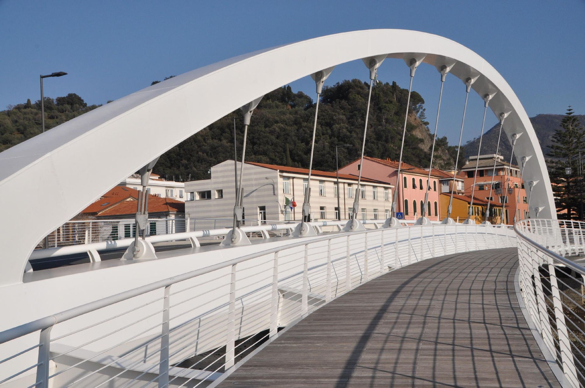 Ponte pedonale ad arco bianco sopra una strada, con edifici sullo sfondo.