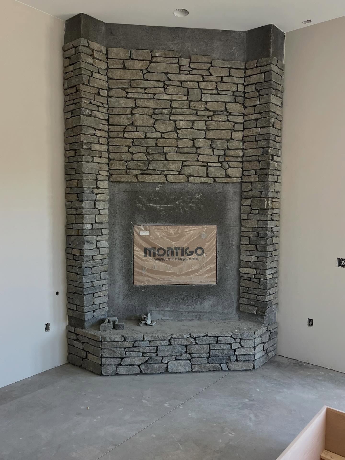 Stone fireplace alcove with a rough-hewn gray stone surround and inset mantel in an unfinished room