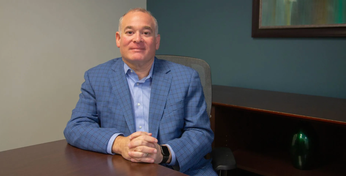 Evan Polin in blue suit sitting at desk. Sales Training EAP Partner Program