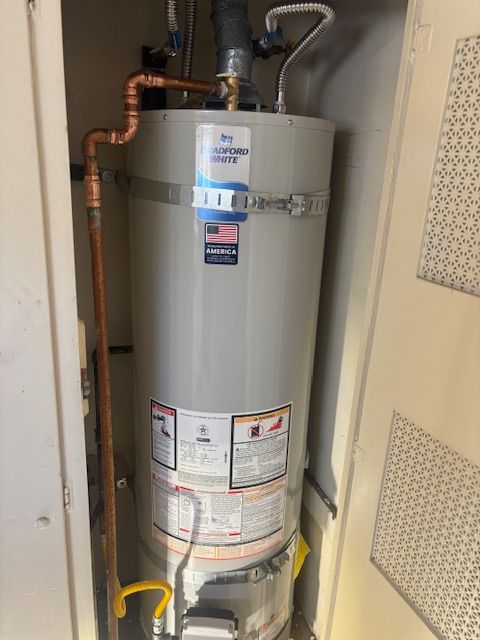 A gas water heater enclosed in a closet with copper pipes and a gas line visible.